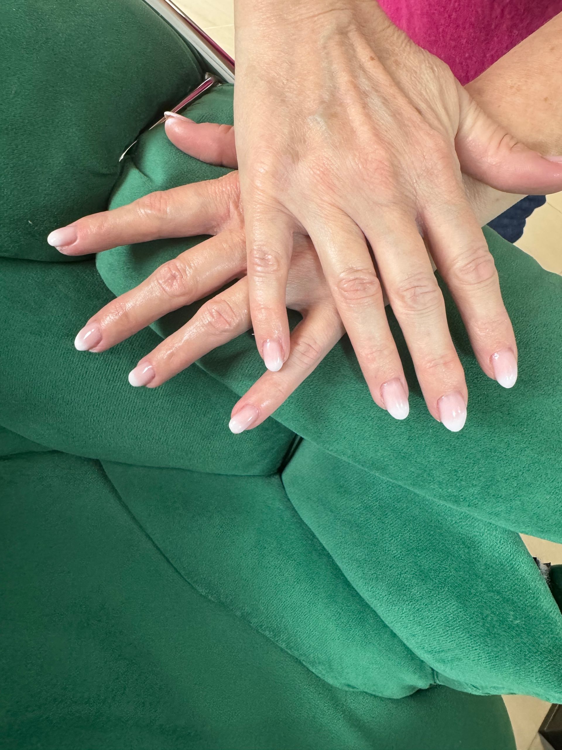 Deux mains superposées posées sur une surface en tissu vert, l'une d'elles montrant de longs ongles pâles