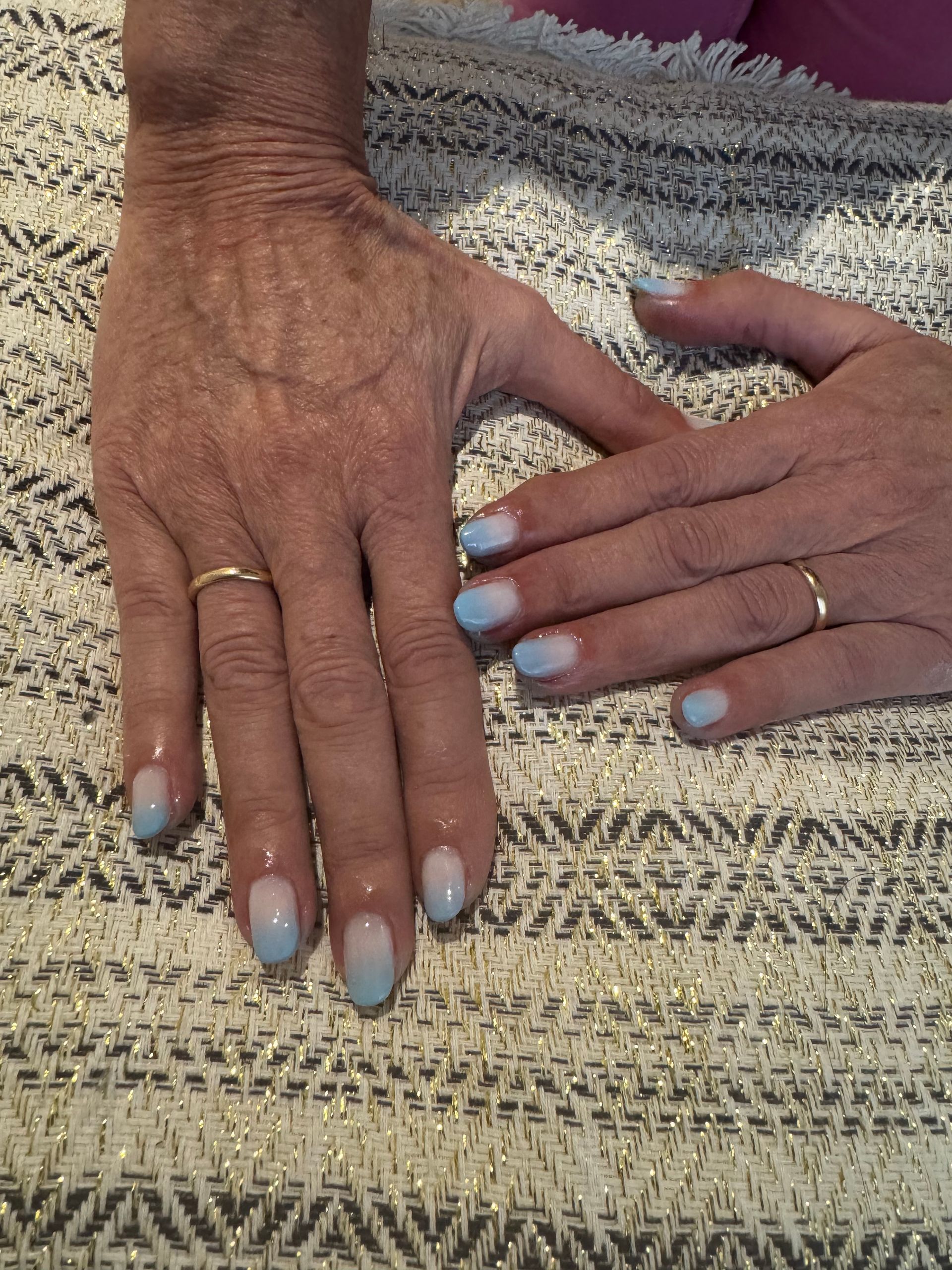 Deux mains aux ongles vernis bleu clair et aux bagues en or reposent sur une couverture tissée