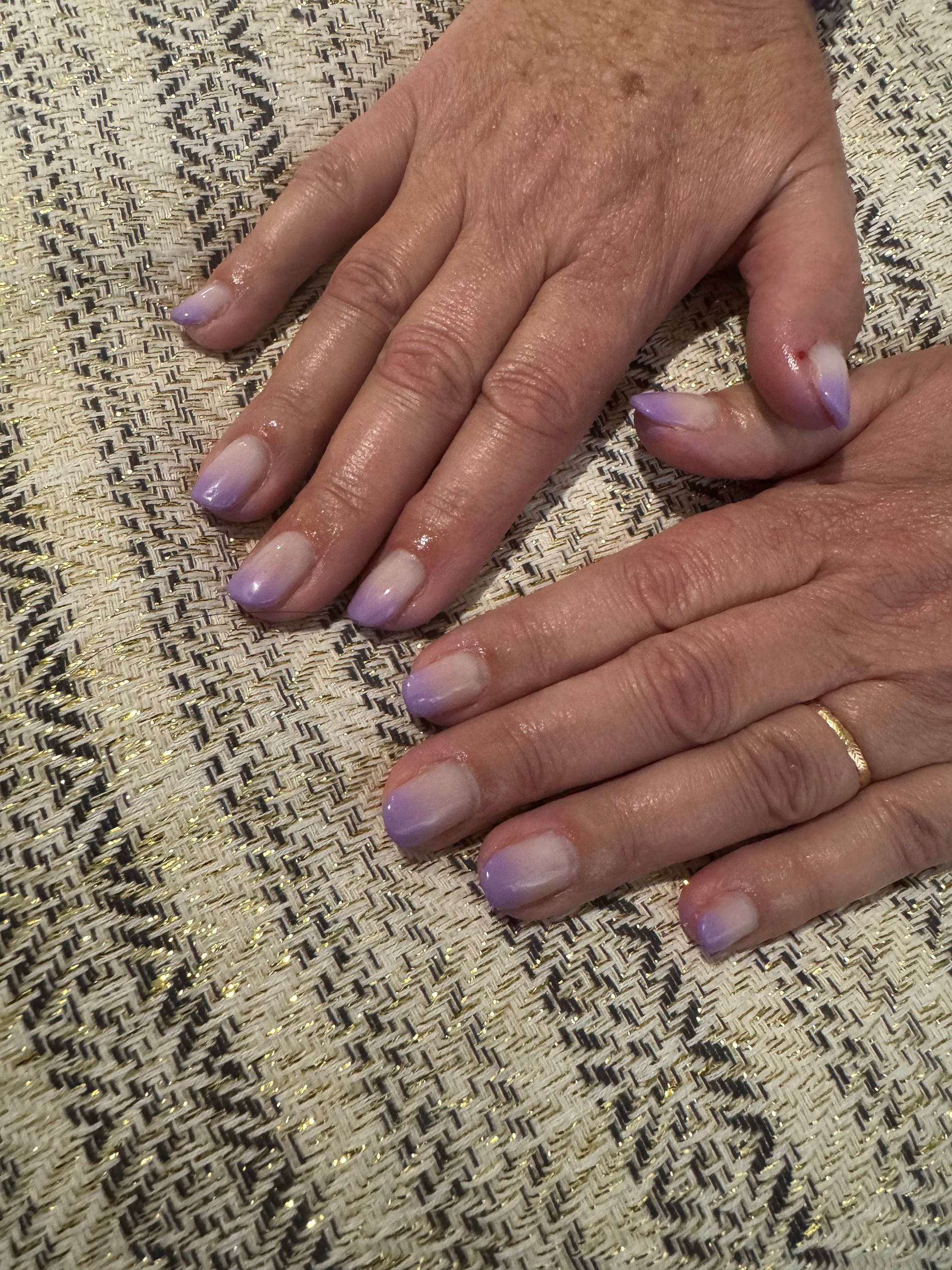 Deux mains aux ongles vernis de lavande posées sur un tissu à motifs tissés.
