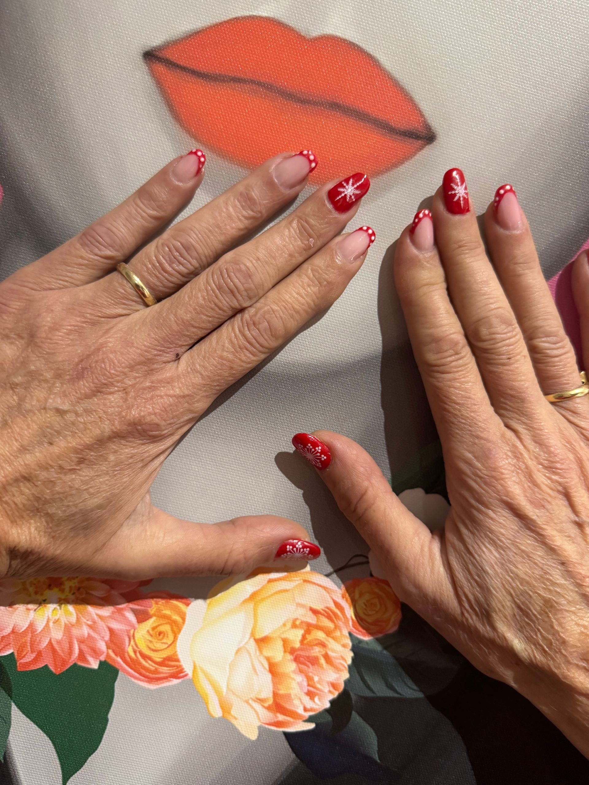 Deux mains aux ongles rouges à motifs floraux encadrent une fresque de lèvres orange sur une chemise à fleurs