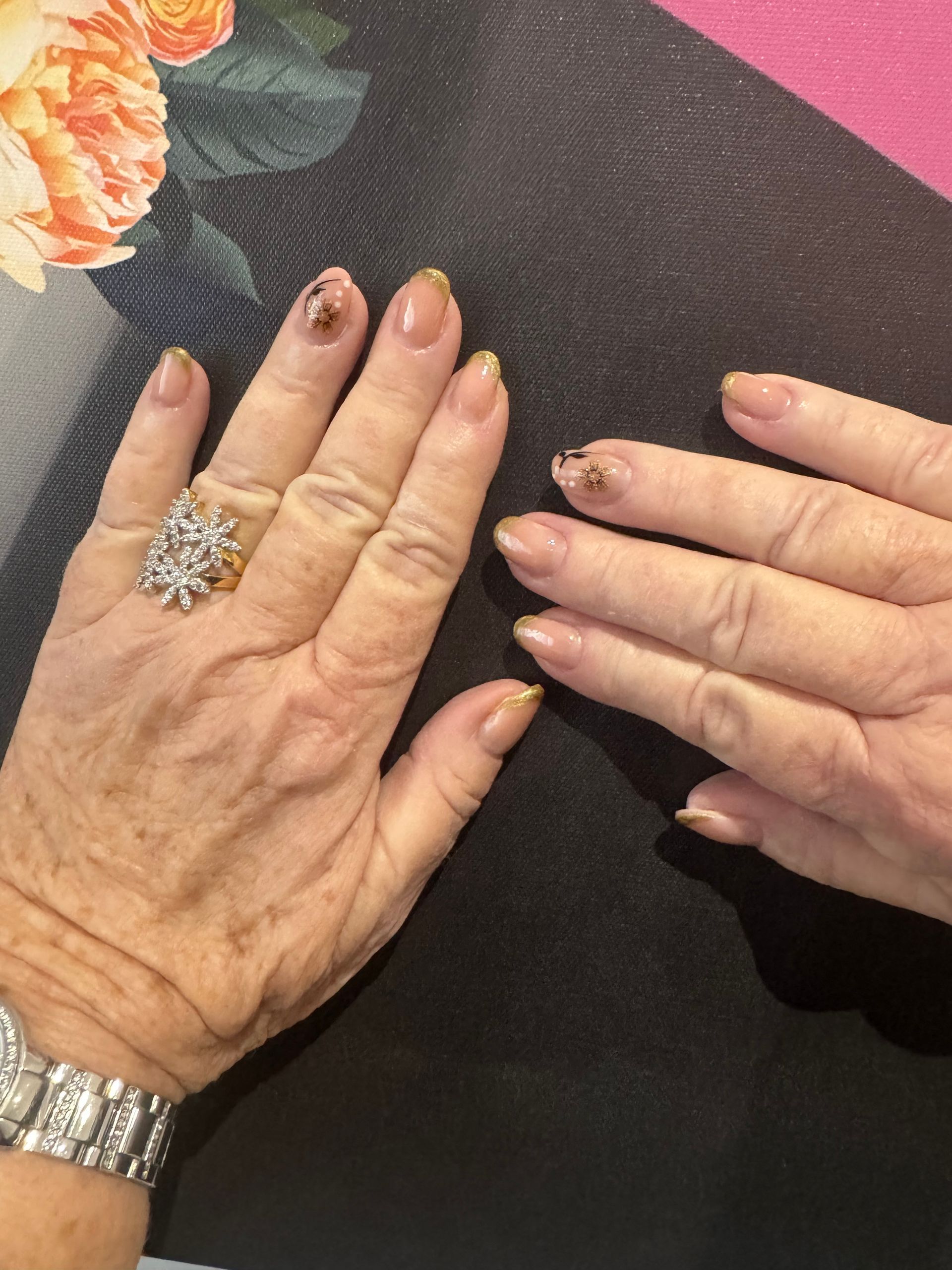 Deux mains posées sur une nappe à motifs floraux sombres, portant une montre et une bague en argent.
