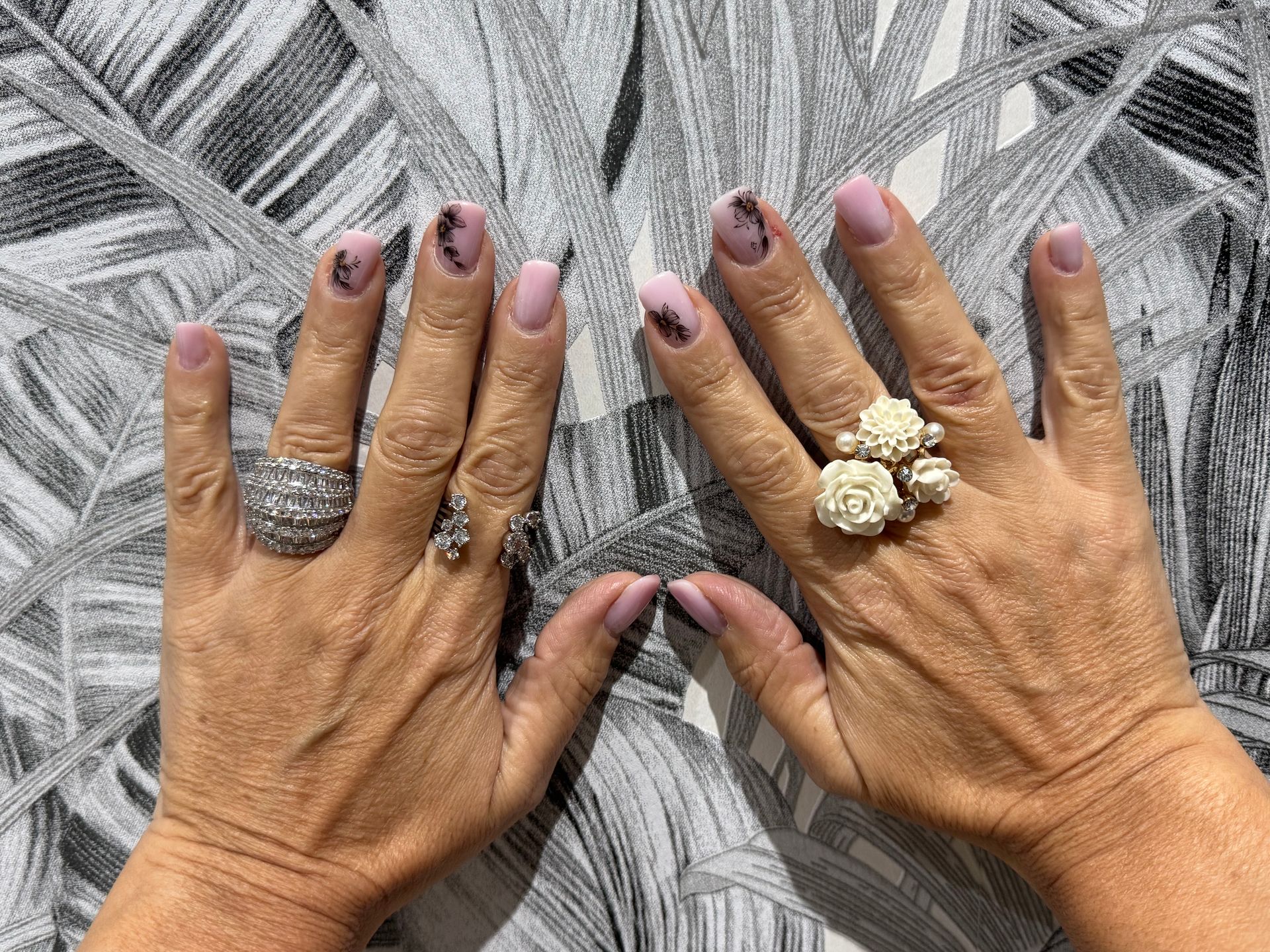 Deux mains ornées de bagues et aux ongles violets reposent sur une surface grise tissée.