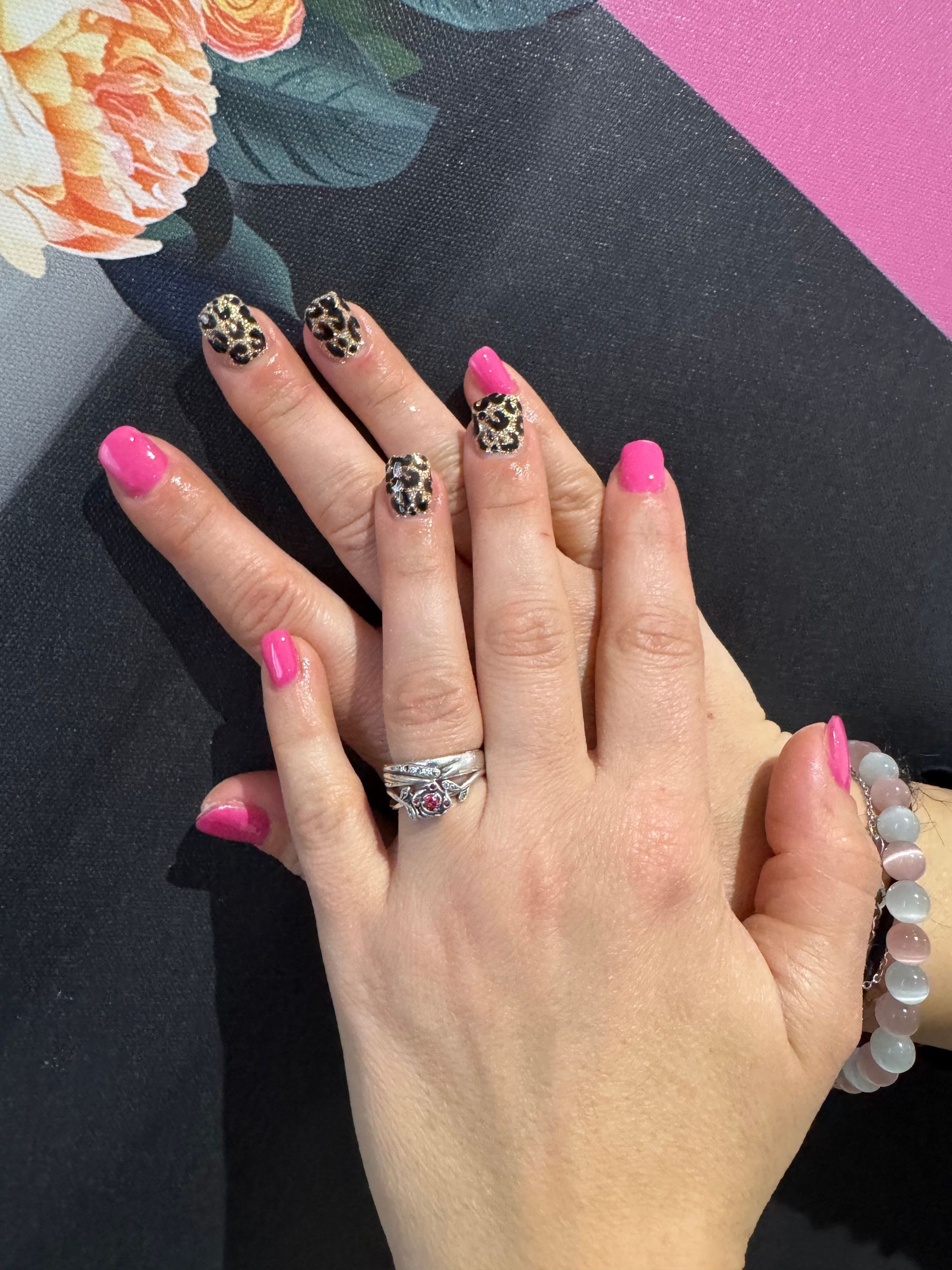 Des mains aux ongles roses et léopard reposent sur une surface sombre ornée d'un motif floral dans un coin.