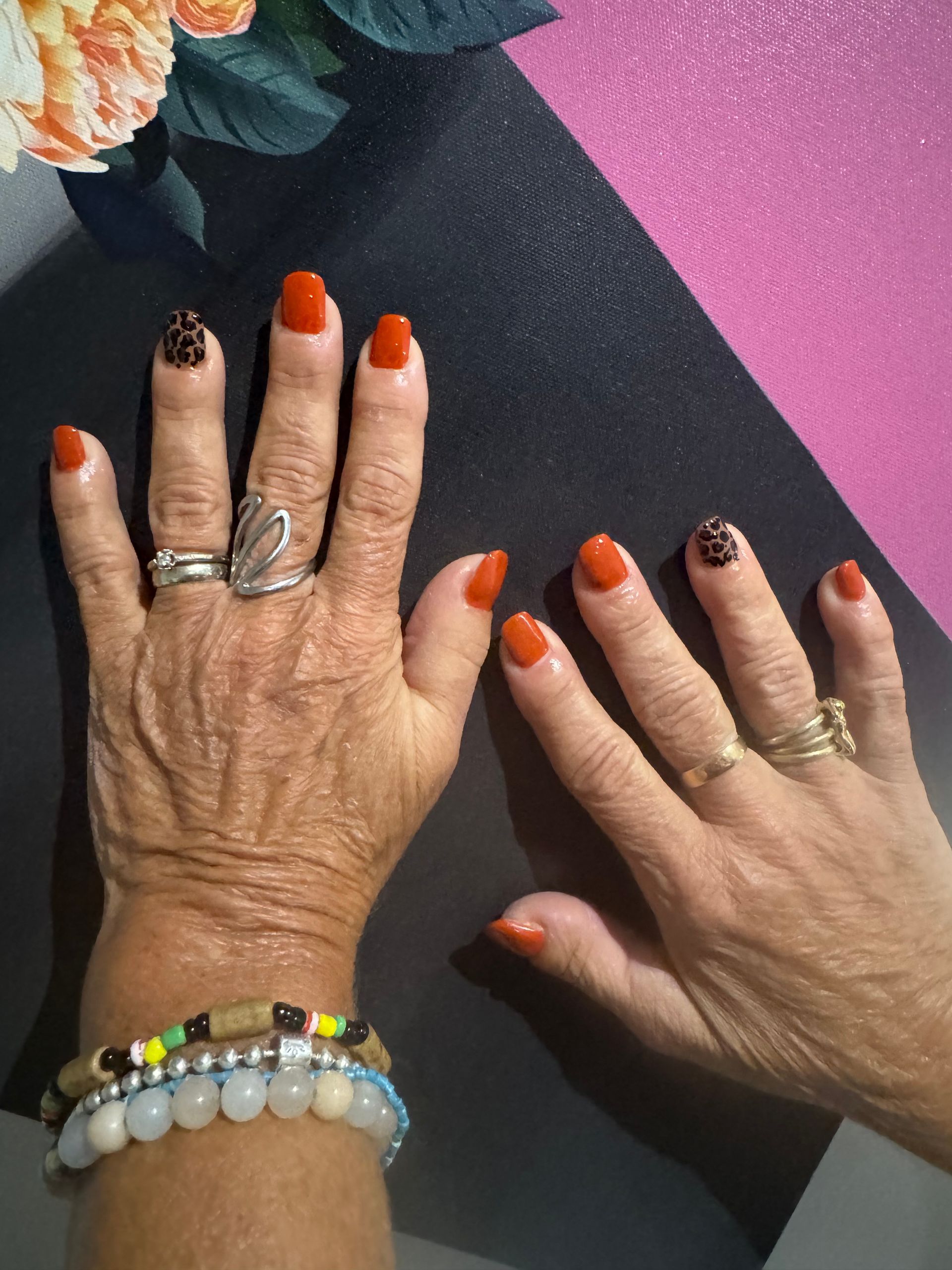 Deux mains aux ongles vernis et aux bagues posées sur une table noire et rose, l'une d'elles portant un bracelet au poignet