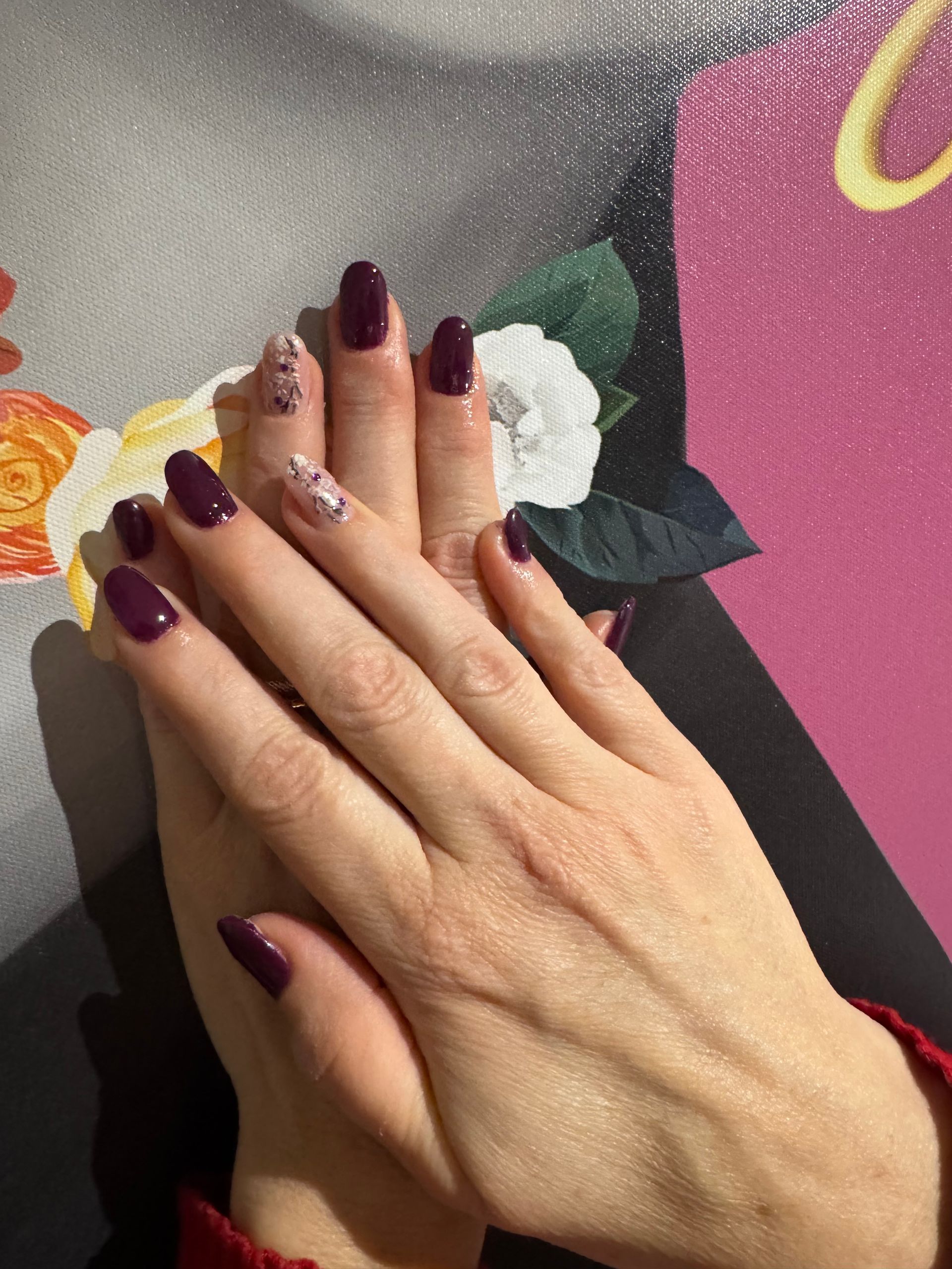 Des mains aux ongles violet foncé reposent sur un fond floral et rose.