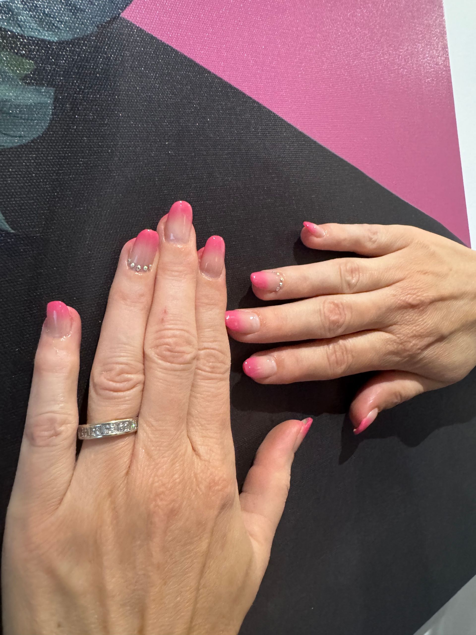 Deux mains aux ongles roses manucurés sur une surface noire et rose
