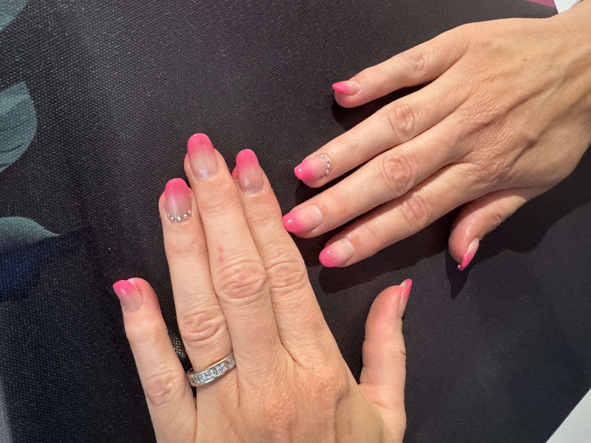 Mains aux ongles roses à la française posées sur un fond de tissu noir