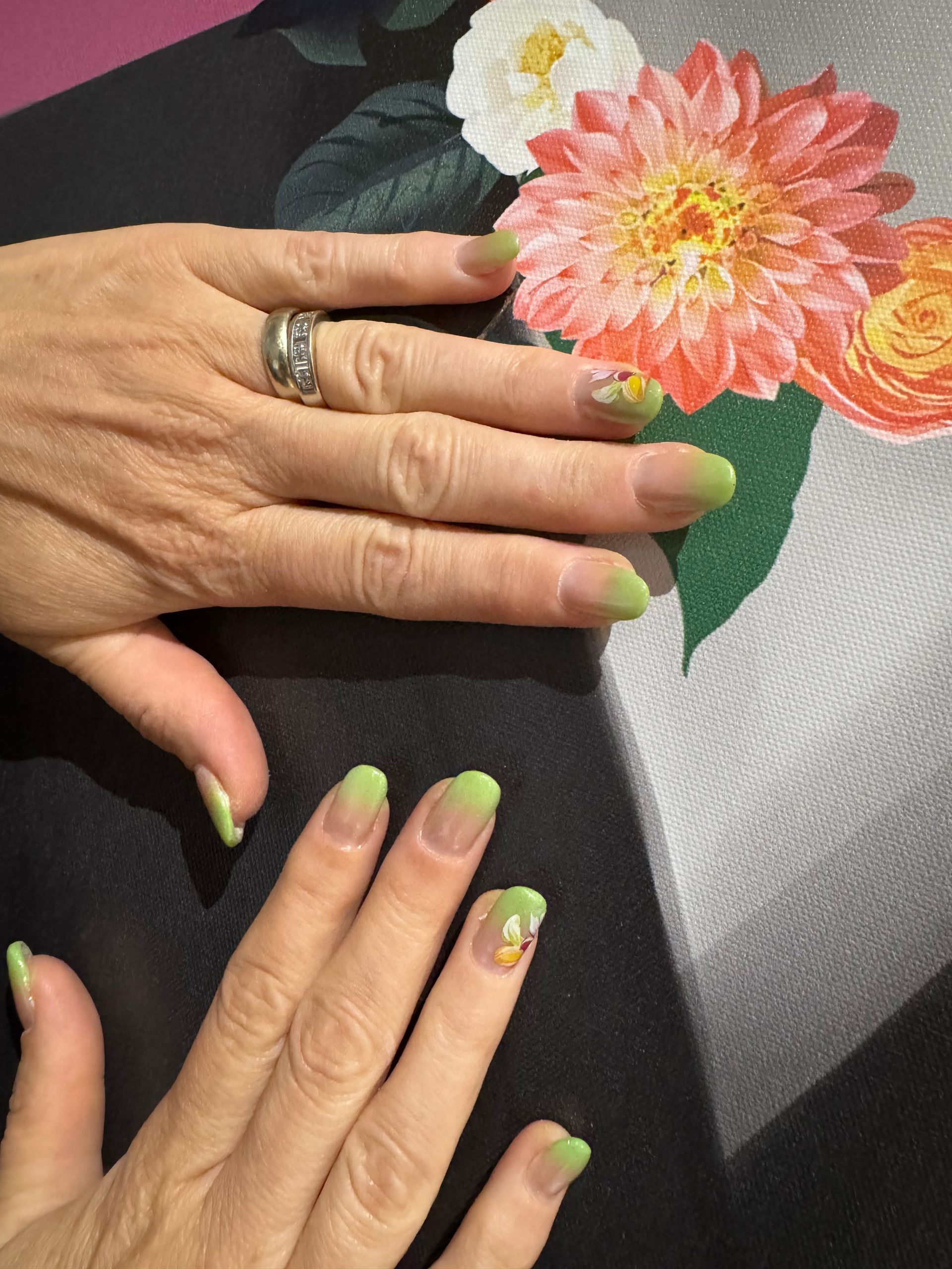 Main aux ongles verts posée sur un tissu noir à côté de fleurs roses et orange