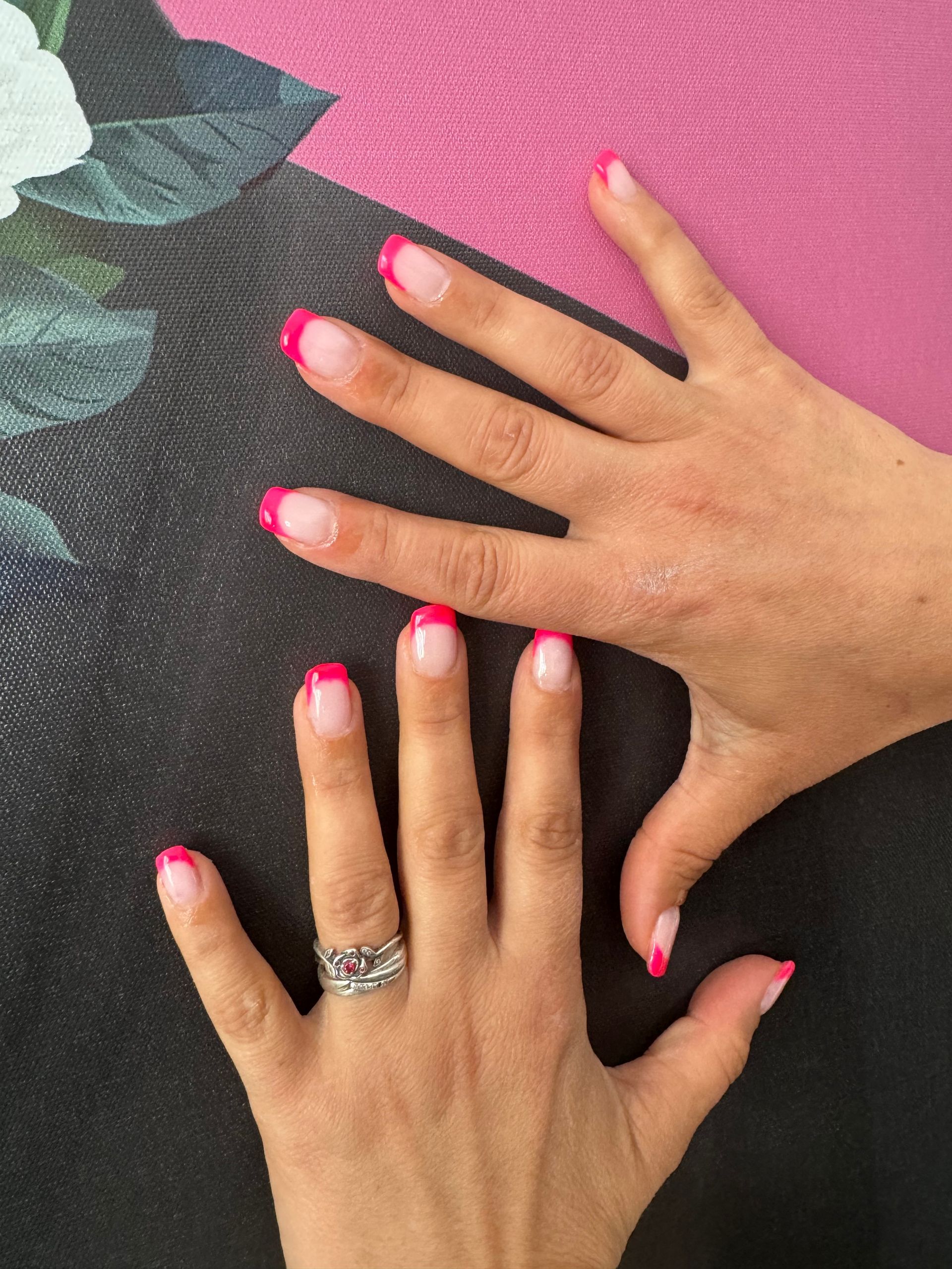 Deux mains avec du vernis à ongles rose vif sur un fond noir et rose