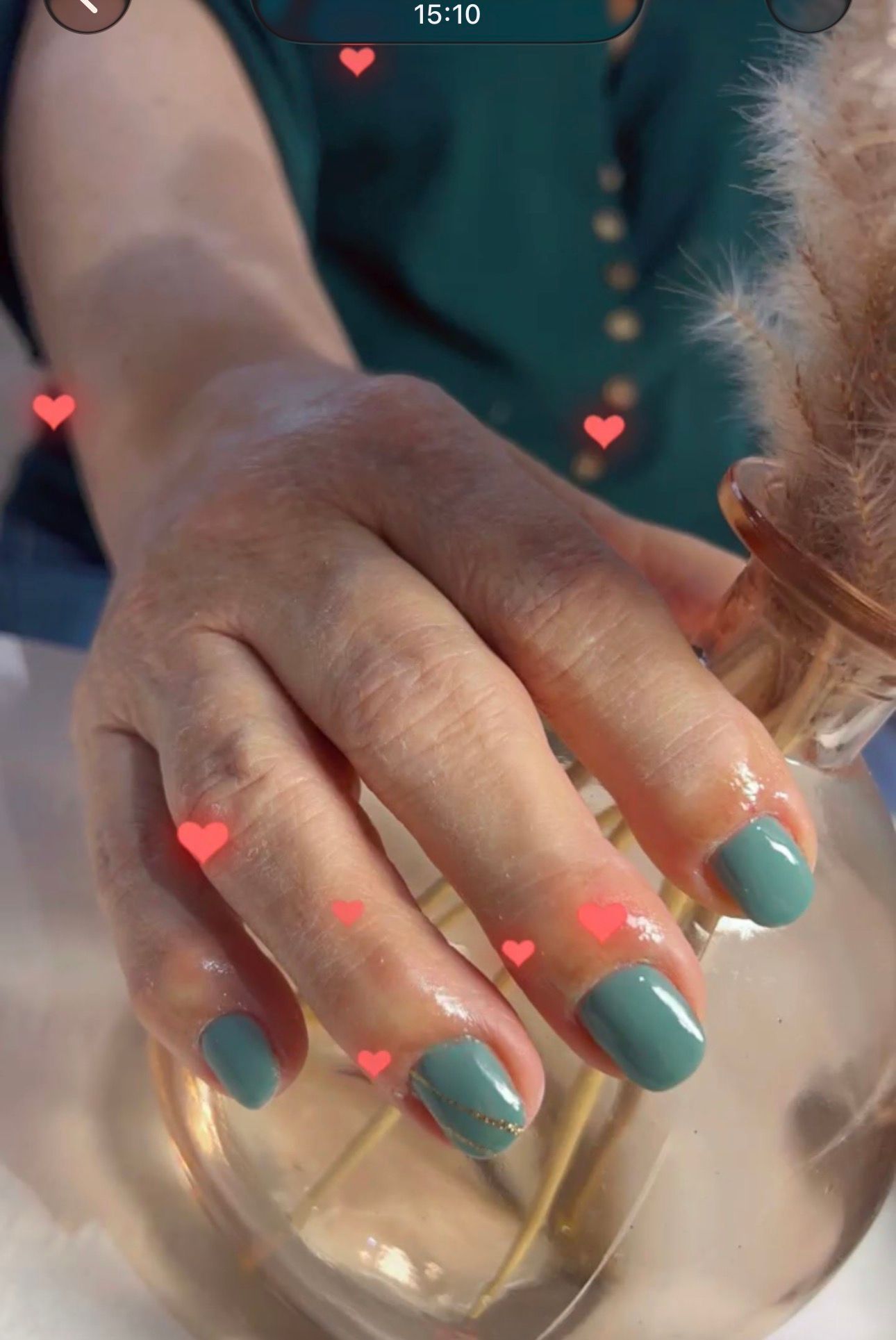 Main aux ongles vernis turquoise posée sur un objet rond en verre transparent, orné de petits cœurs roses.