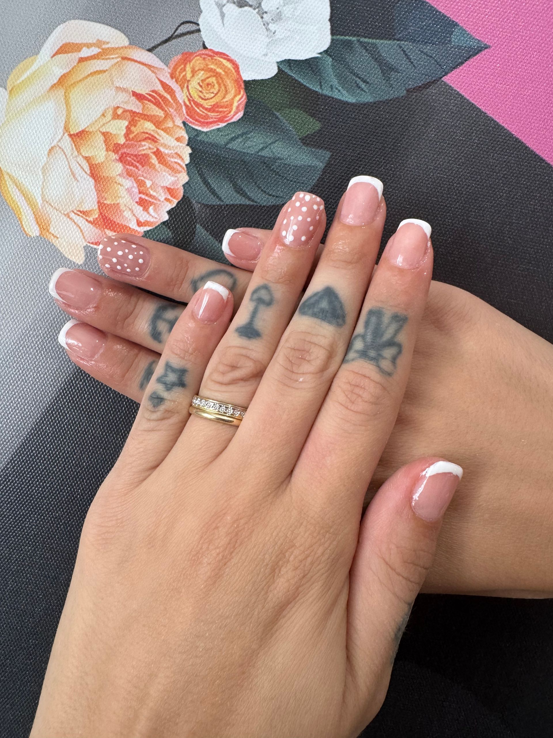 Mains avec des ongles décorés de motifs floraux et une bague au-dessus d'un carnet à motifs floraux noirs sur fond rose