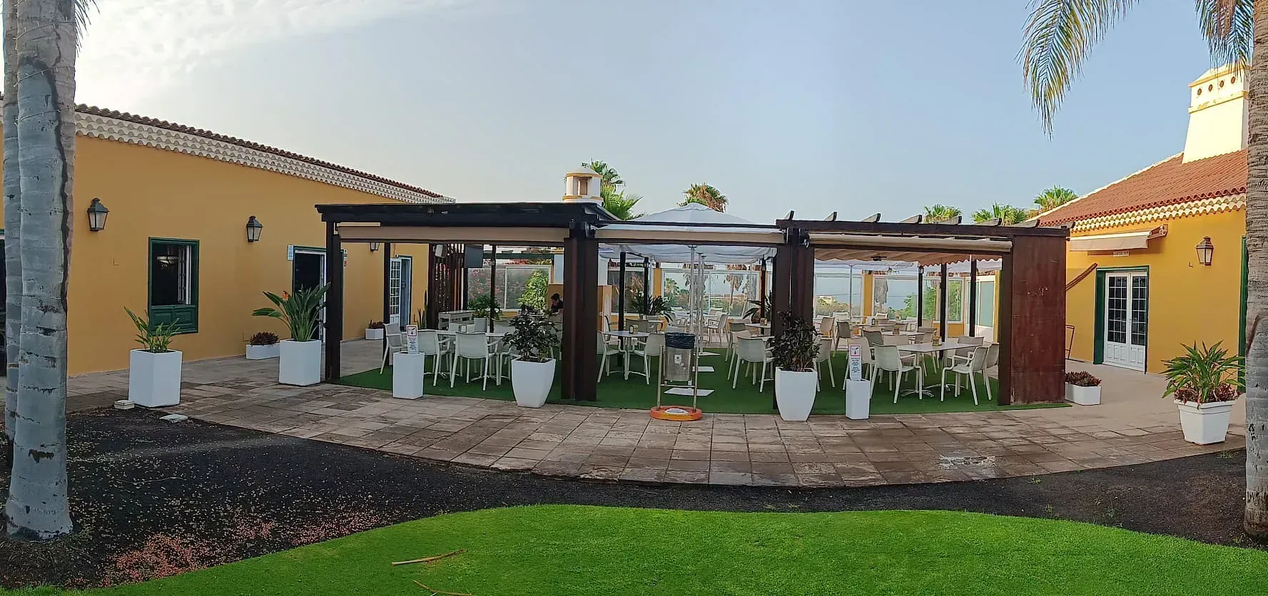 Un patio con mesas y sillas frente a un edificio amarillo.