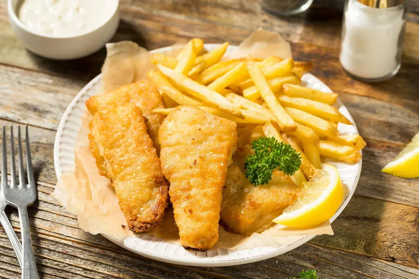 Un plato blanco cubierto con pescado y papas fritas sobre una mesa de madera.