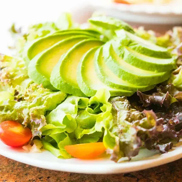 Un plato blanco cubierto con rodajas de aguacate, lechuga y tomates.