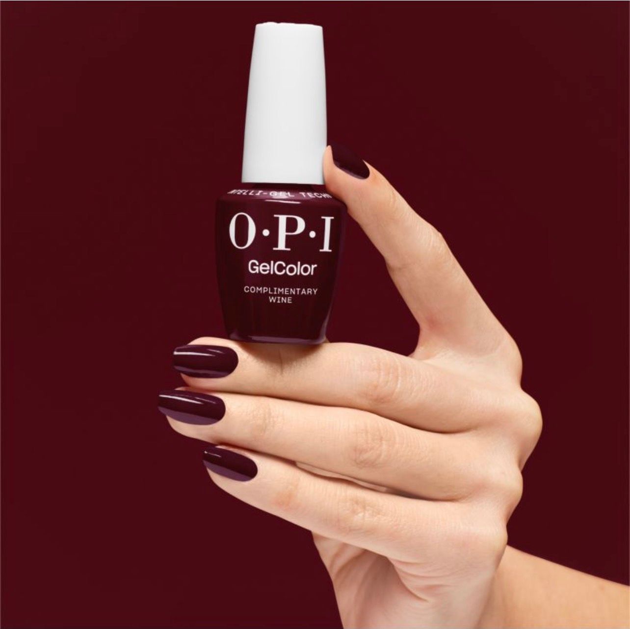 Main tenant un flacon de vernis à ongles OPI GelColor rouge foncé, ongles vernis.