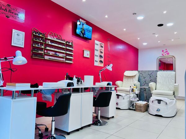 Intérieur d'un salon de manucure avec des murs roses, des tables de manucure, des fauteuils de pédicure et un présentoir de vernis à ongles.