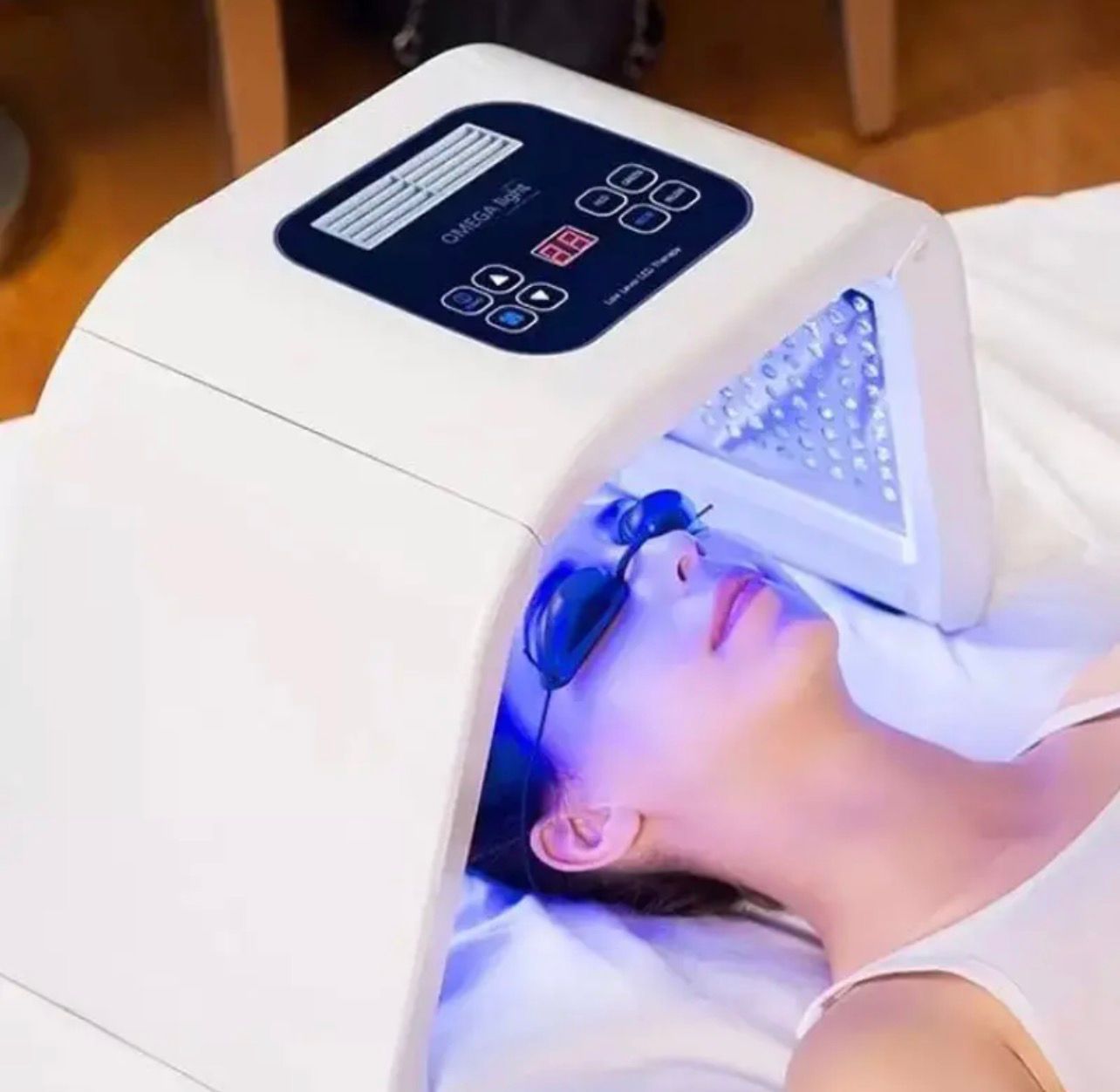 Femme recevant un traitement de luminothérapie à la lumière bleue avec des lunettes de protection dans un spa.