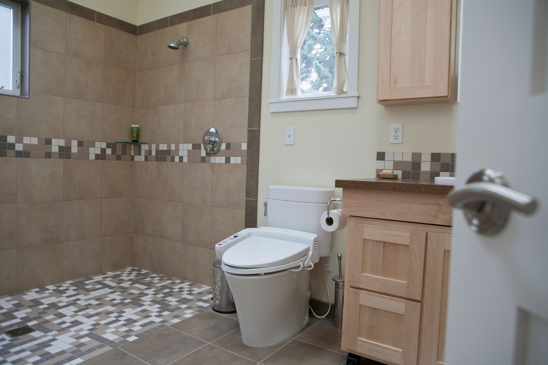 Salle de bains moderne avec douche carrelée, toilettes et meuble-lavabo en bois près d’une fenêtre.