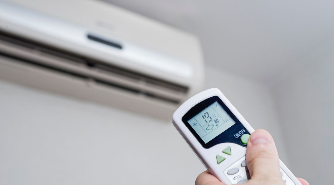 Une main tenant une télécommande dirigée vers un climatiseur mural pour régler la température.