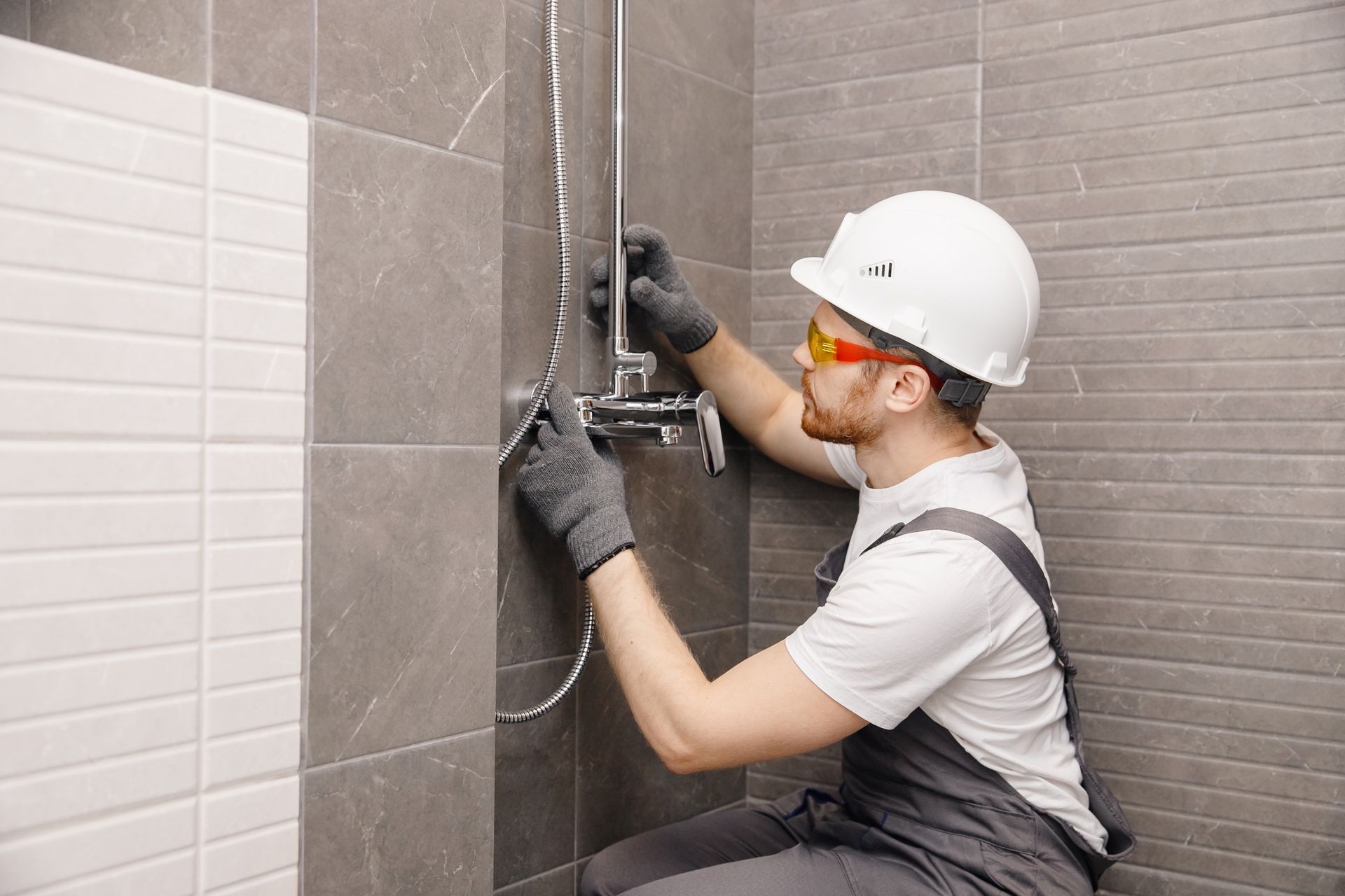 Un ouvrier portant un casque installe des équipements de douche sur un mur de salle de bains carrelé.