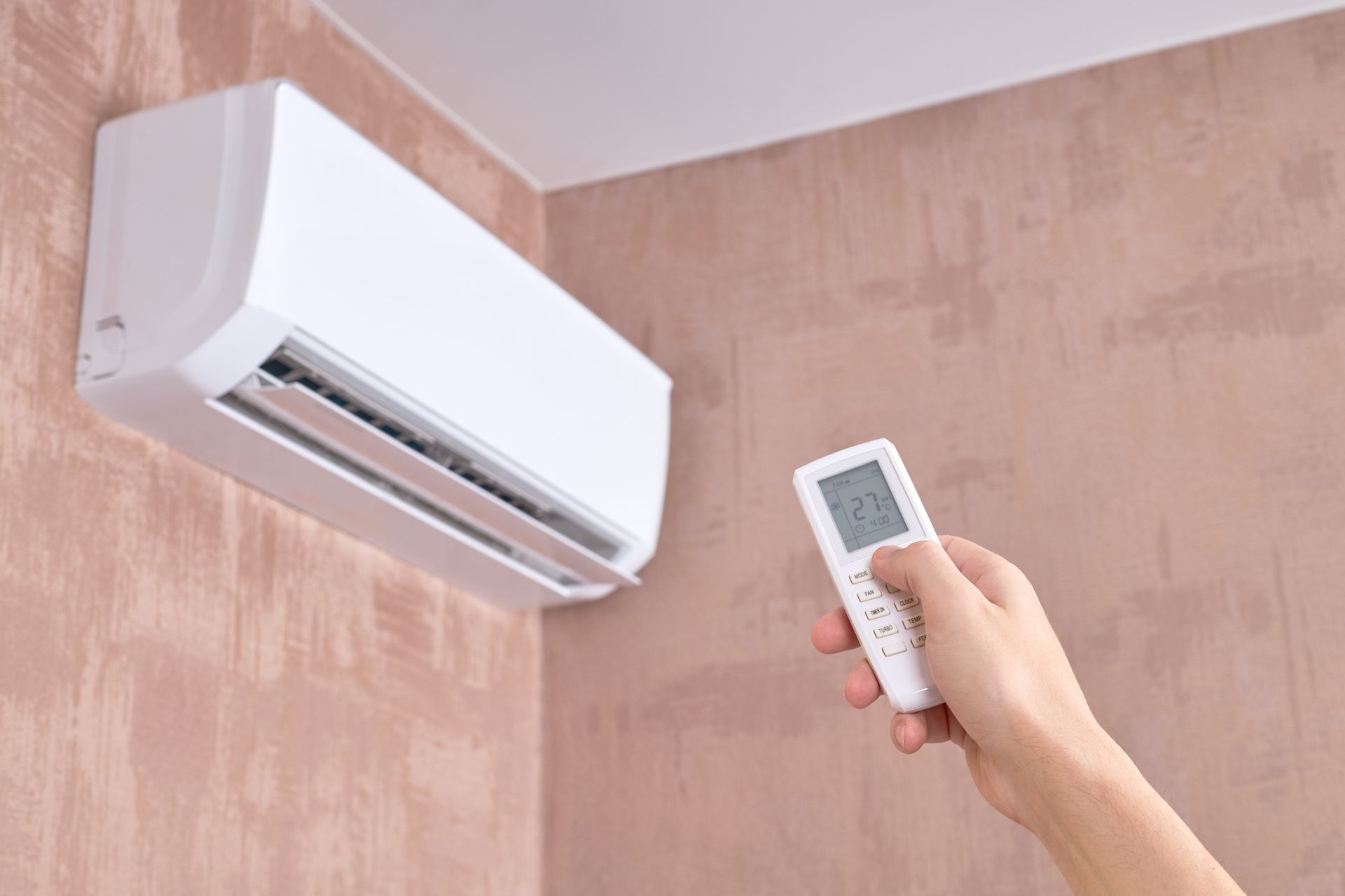 Une main tenant une télécommande pointée vers un climatiseur mural dans une pièce.