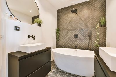 Salle de bains moderne avec baignoire îlot, meuble vasque noir, miroir rond et mur carrelé texturé.