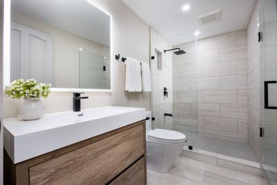 Salle de bains moderne avec meuble-lavabo suspendu en bois, grand miroir et douche à paroi vitrée.
