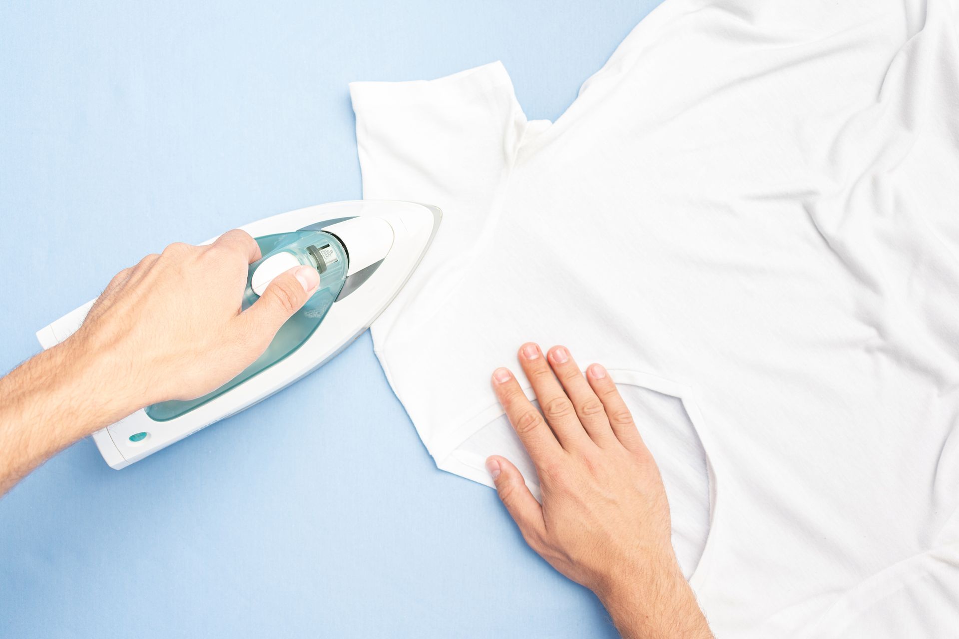 Une personne utilise un fer pour repasser le col d'une chemise blanche sur une surface bleu clair.