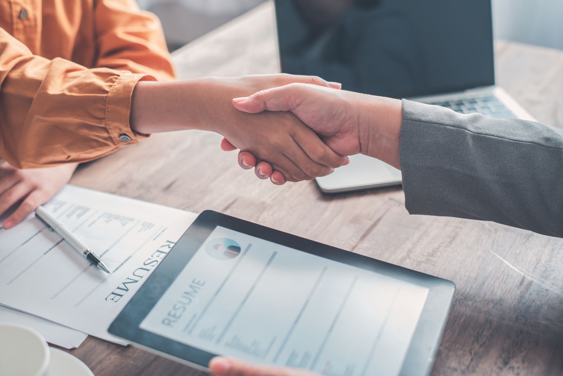 Deux personnes se serrent la main au-dessus d'une table où se trouve un CV.