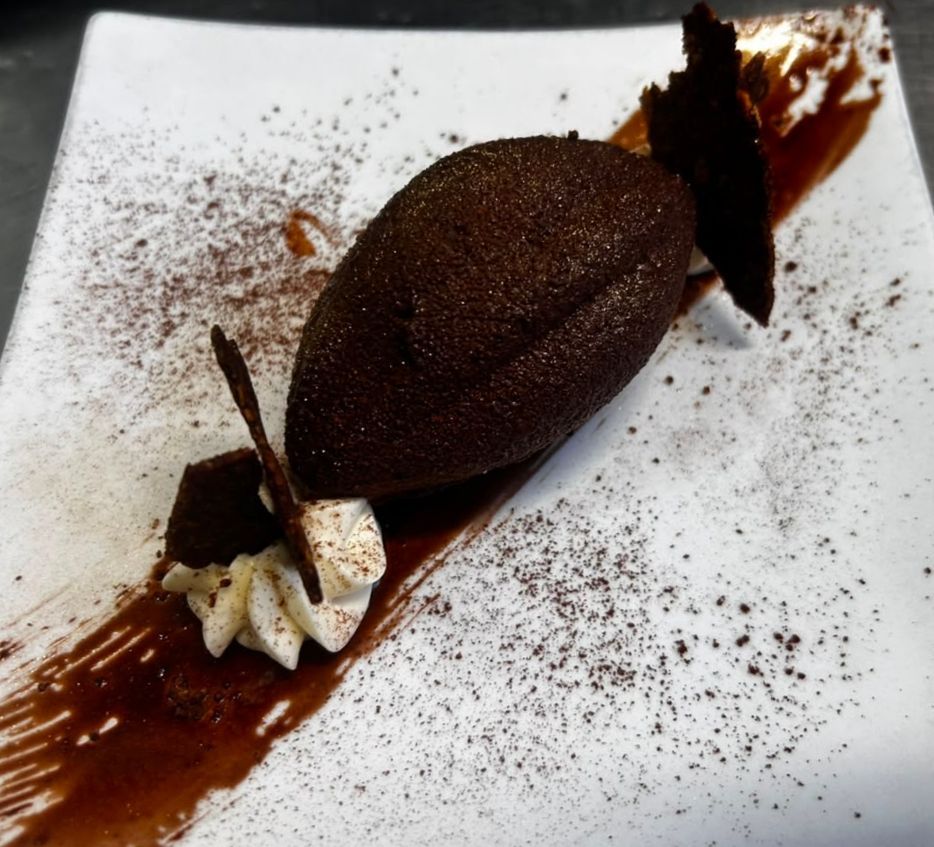 Gâteau au chocolat avec glaçage blanc, noix et cacao en poudre, présenté sur une assiette blanche.