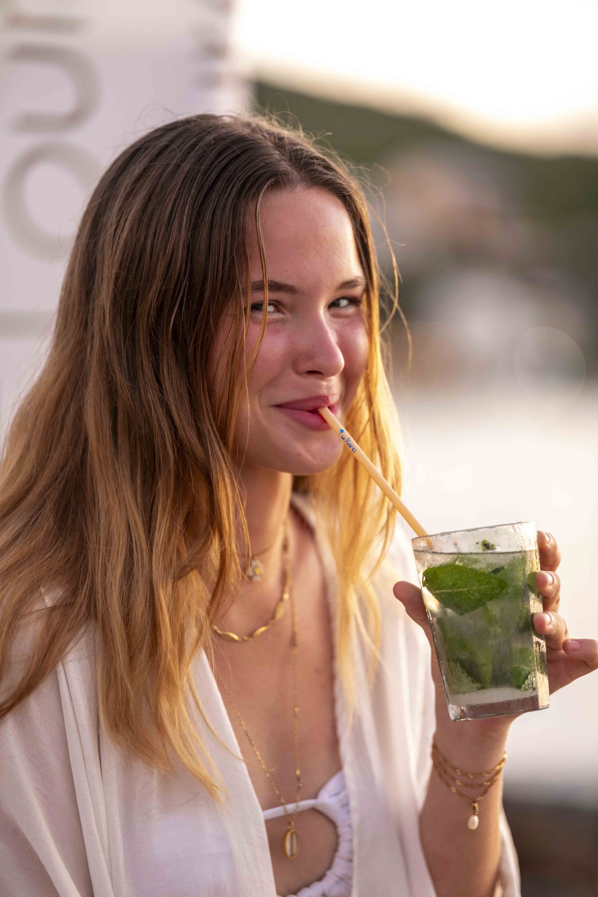 Une jeune femme boit un cocktail en souriant