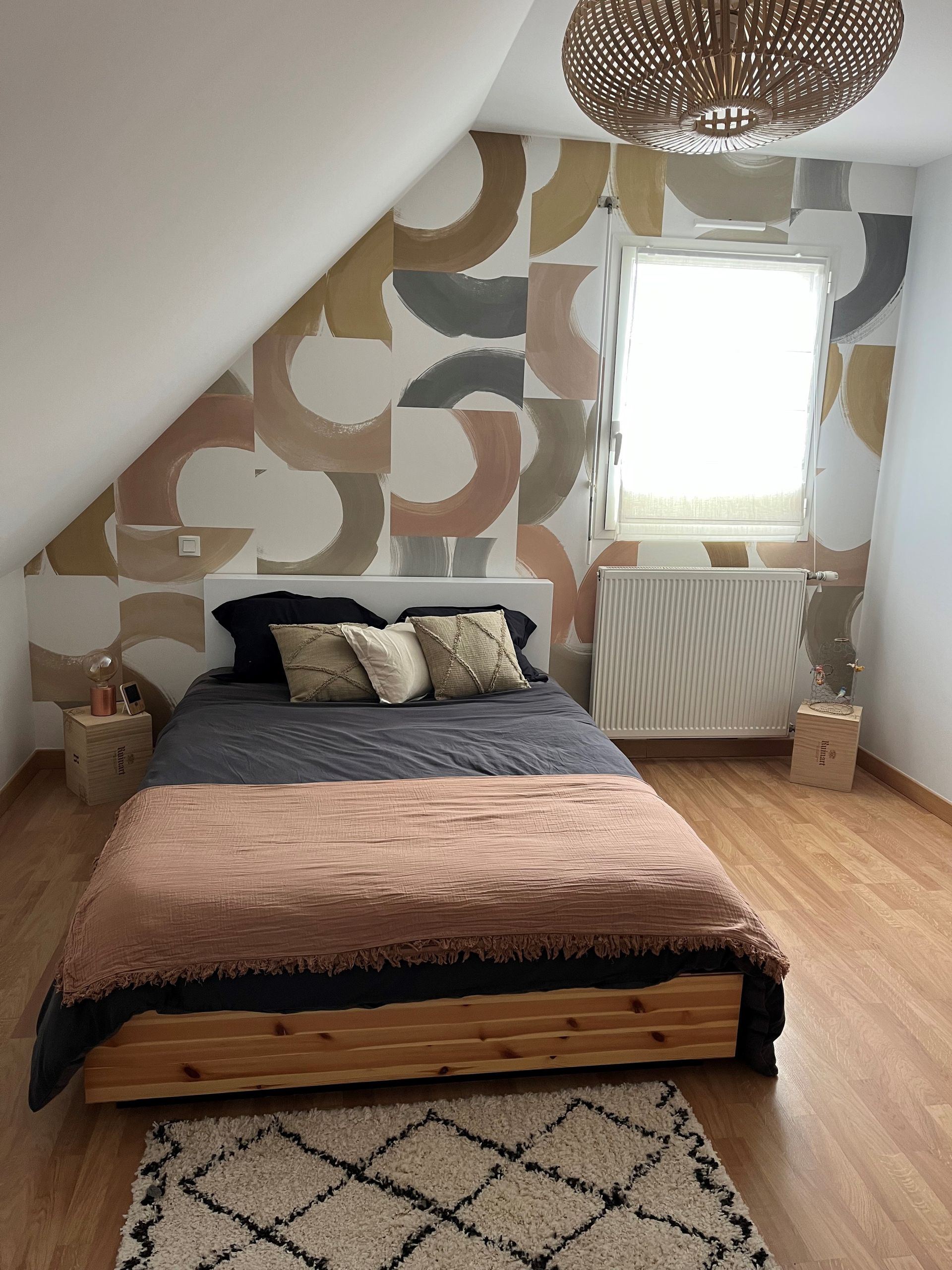 Chambre mansardée confortable avec un lit en bois, un mur d'accent à motifs, une fenêtre de toit et un tapis sur parquet.