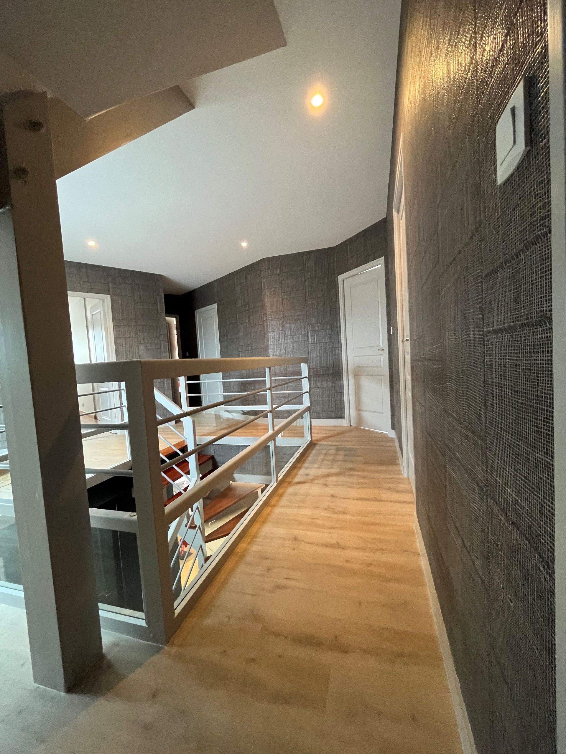Couloir de loft moderne avec parquet, murs texturés foncés et rambarde blanche donnant sur le niveau inférieur