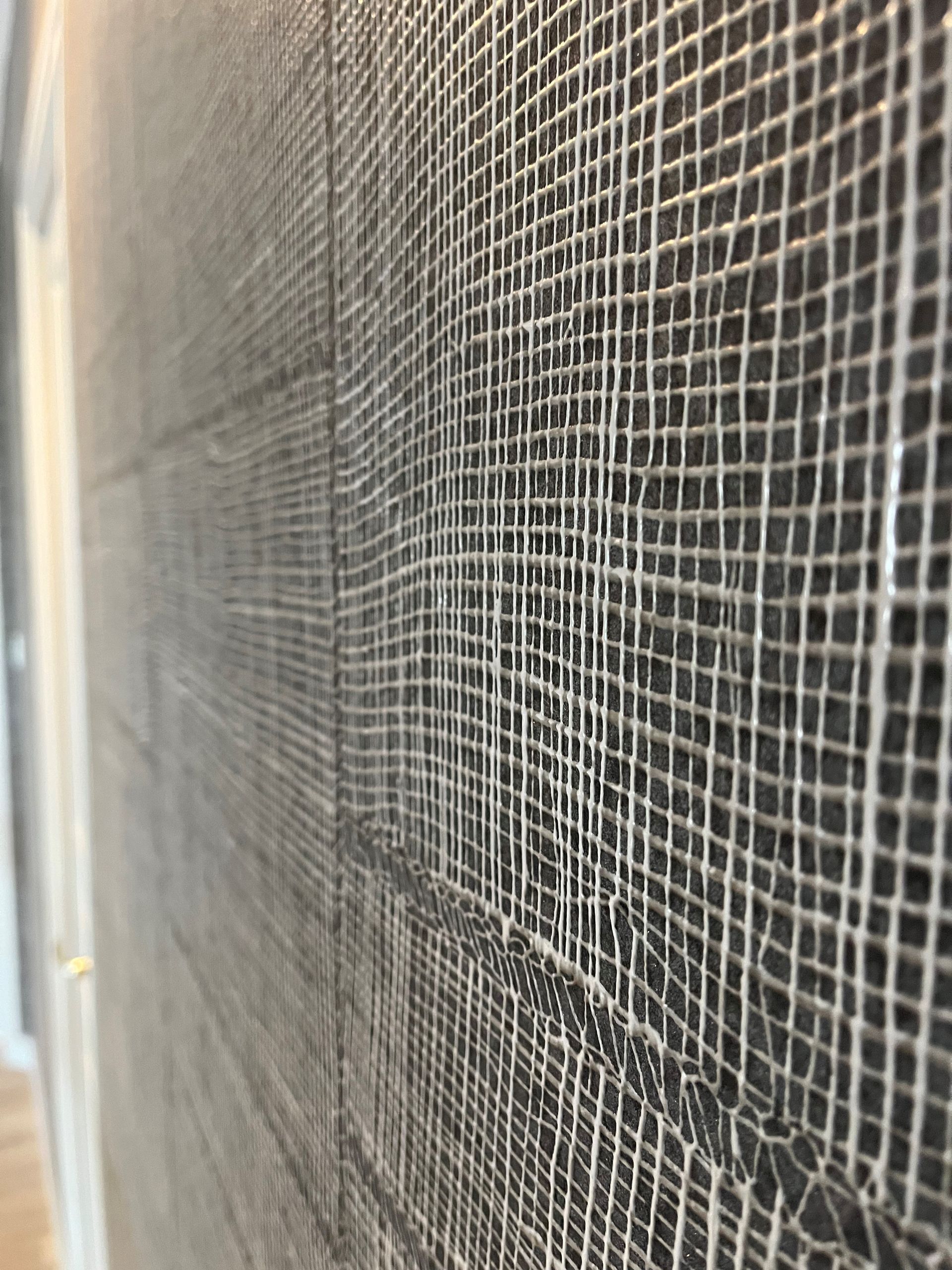 Gros plan sur une moustiquaire sombre avec un bord clair à gauche, révélant un fin motif de grille.