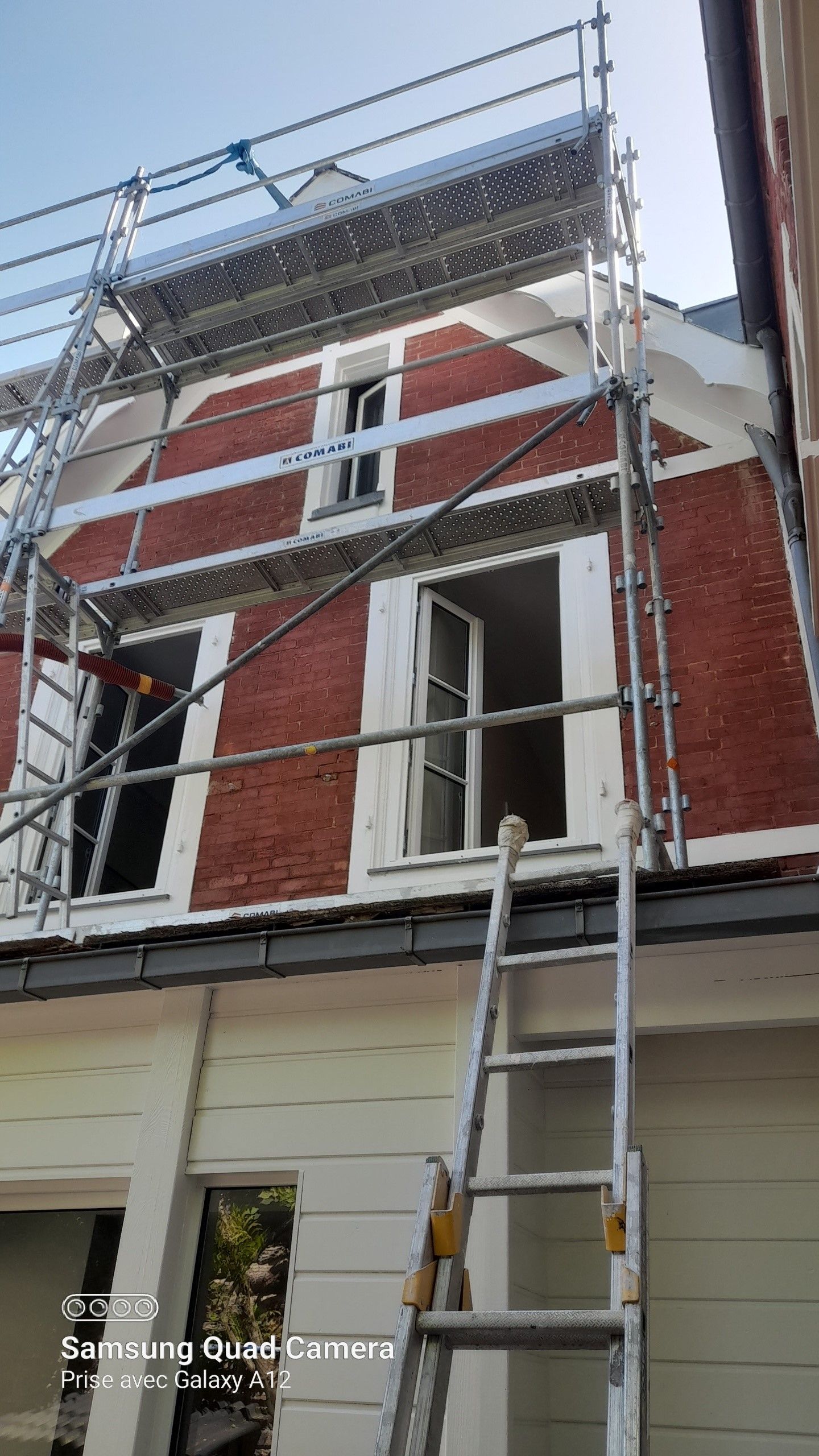 Échafaudages et échelles sur une maison en briques rouges aux boiseries blanches en cours de rénovation