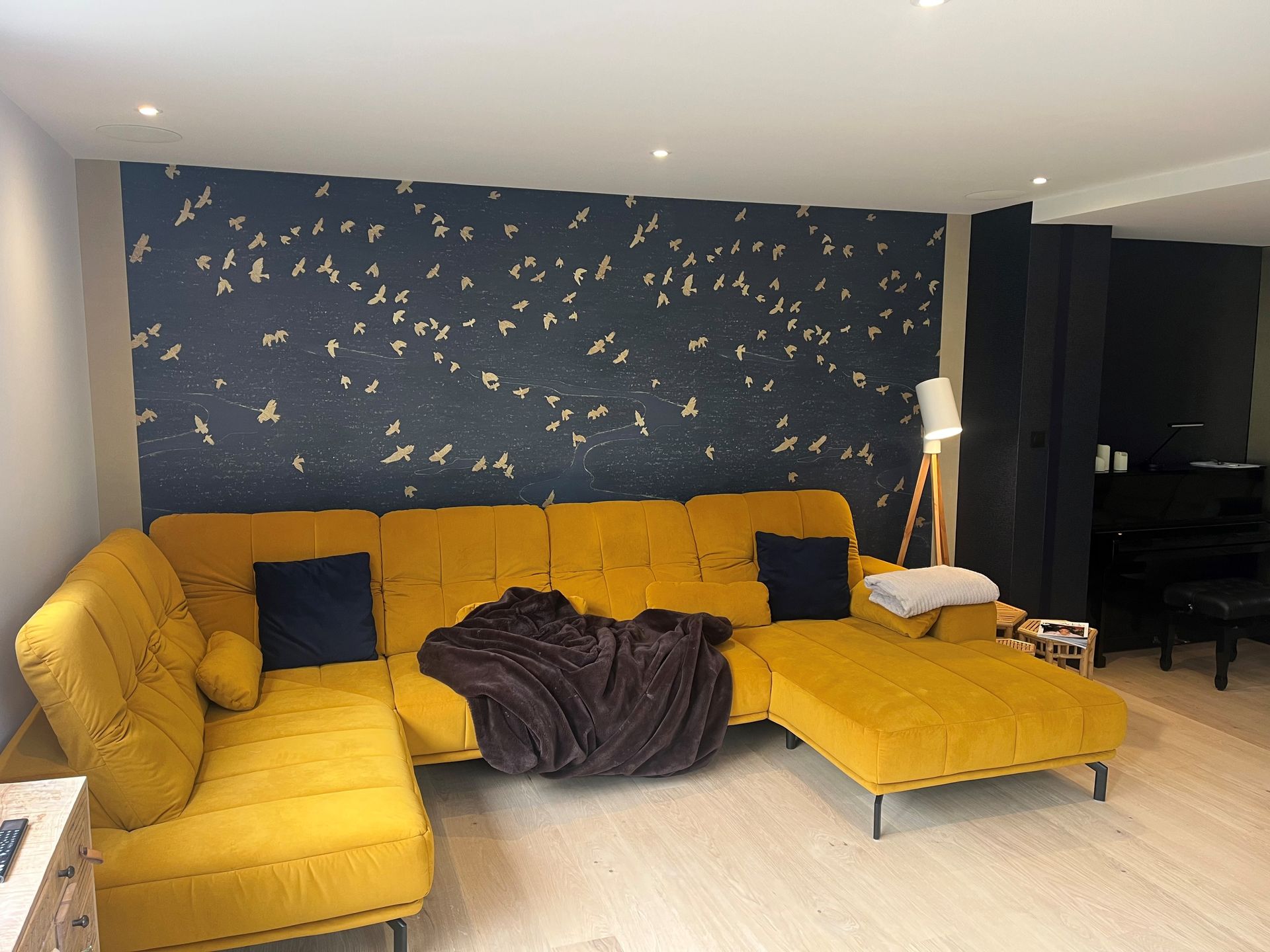 Canapé d'angle jaune vif dans un salon moderne avec papier peint à motifs foncés et lampadaire.