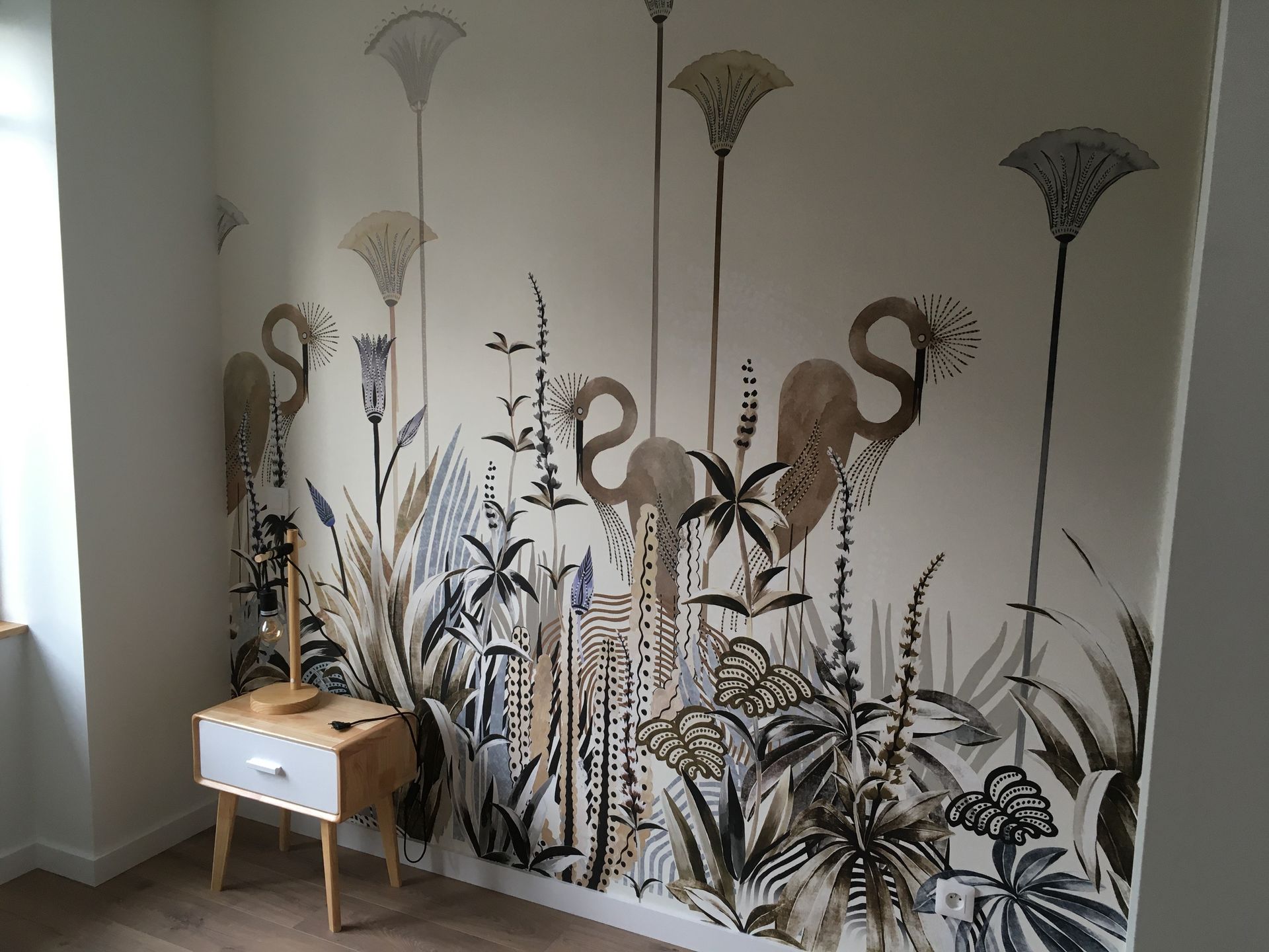 Des fresques de flamants roses et de plantes tropicales ornent un mur blanc à côté d'une petite table en bois.