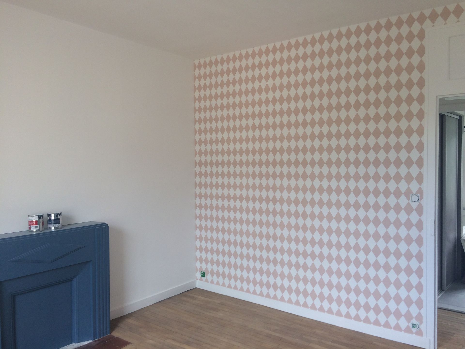 Pièce vide avec papier peint à motifs roses, murs blancs, parquet et cheminée bleu foncé.