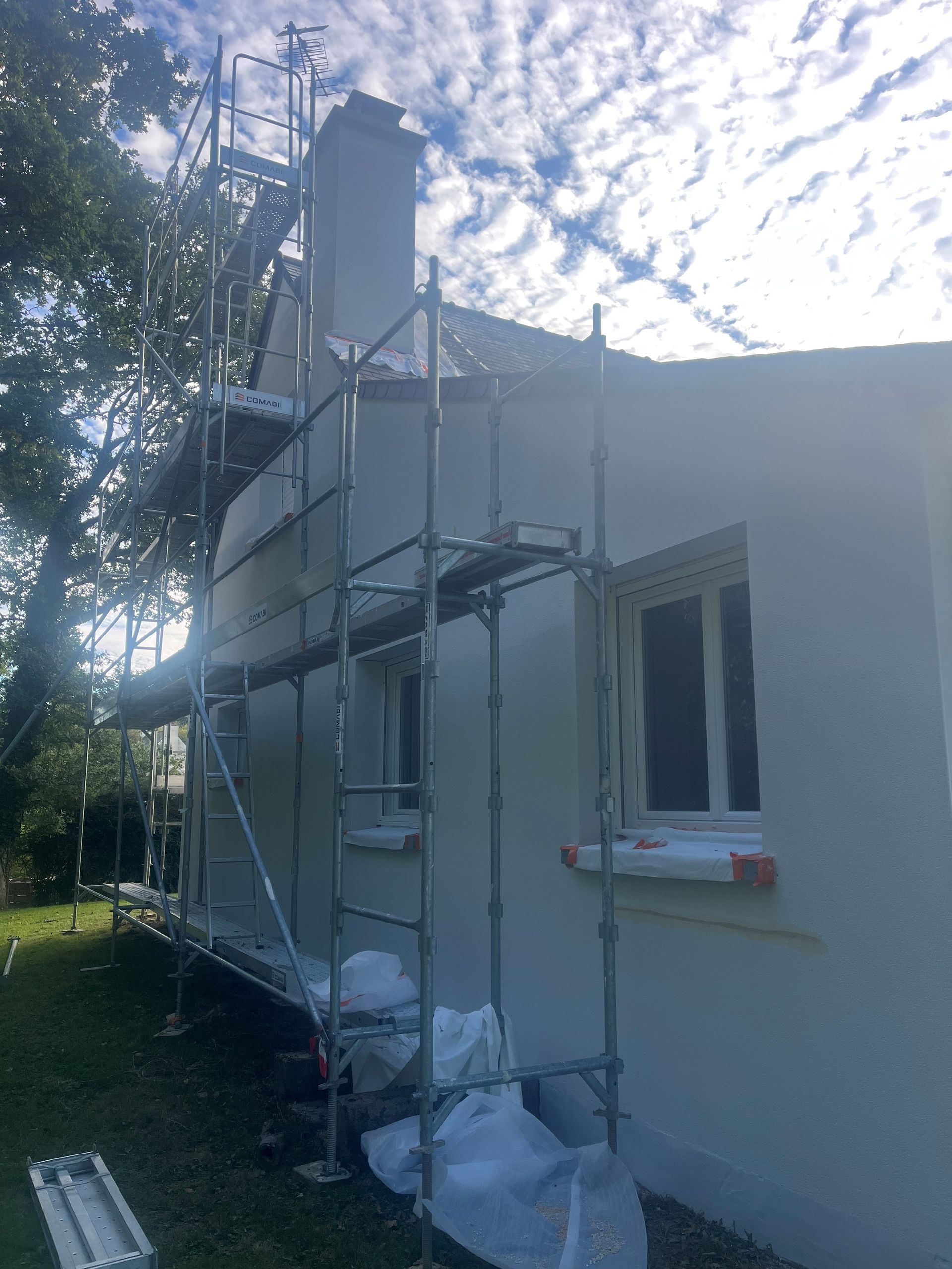 Échafaudage à côté de la façade d'une maison blanche sous un ciel lumineux et nuageux