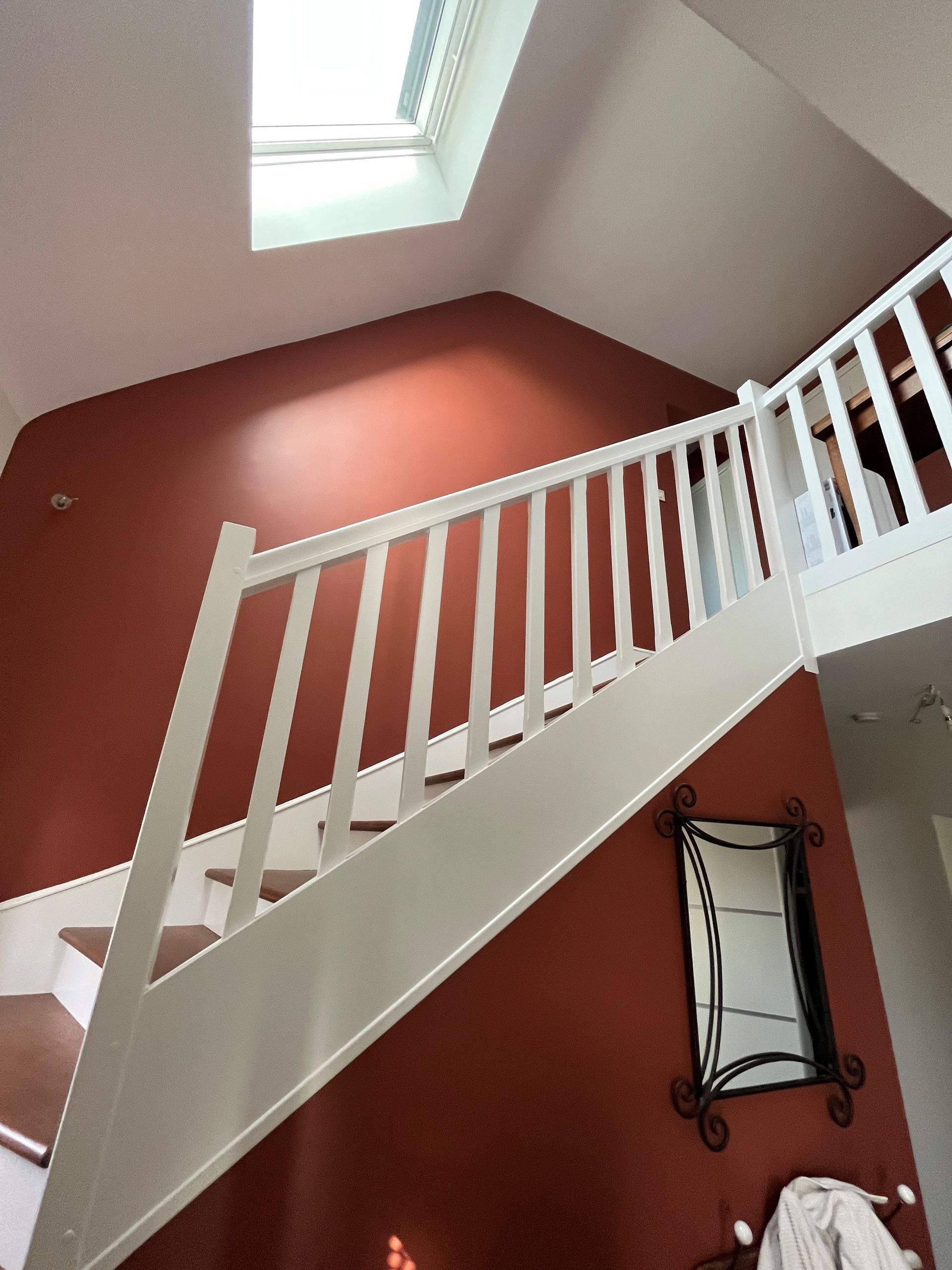Un escalier blanc se détachant sur un mur rouge sous une verrière dans un intérieur de maison
