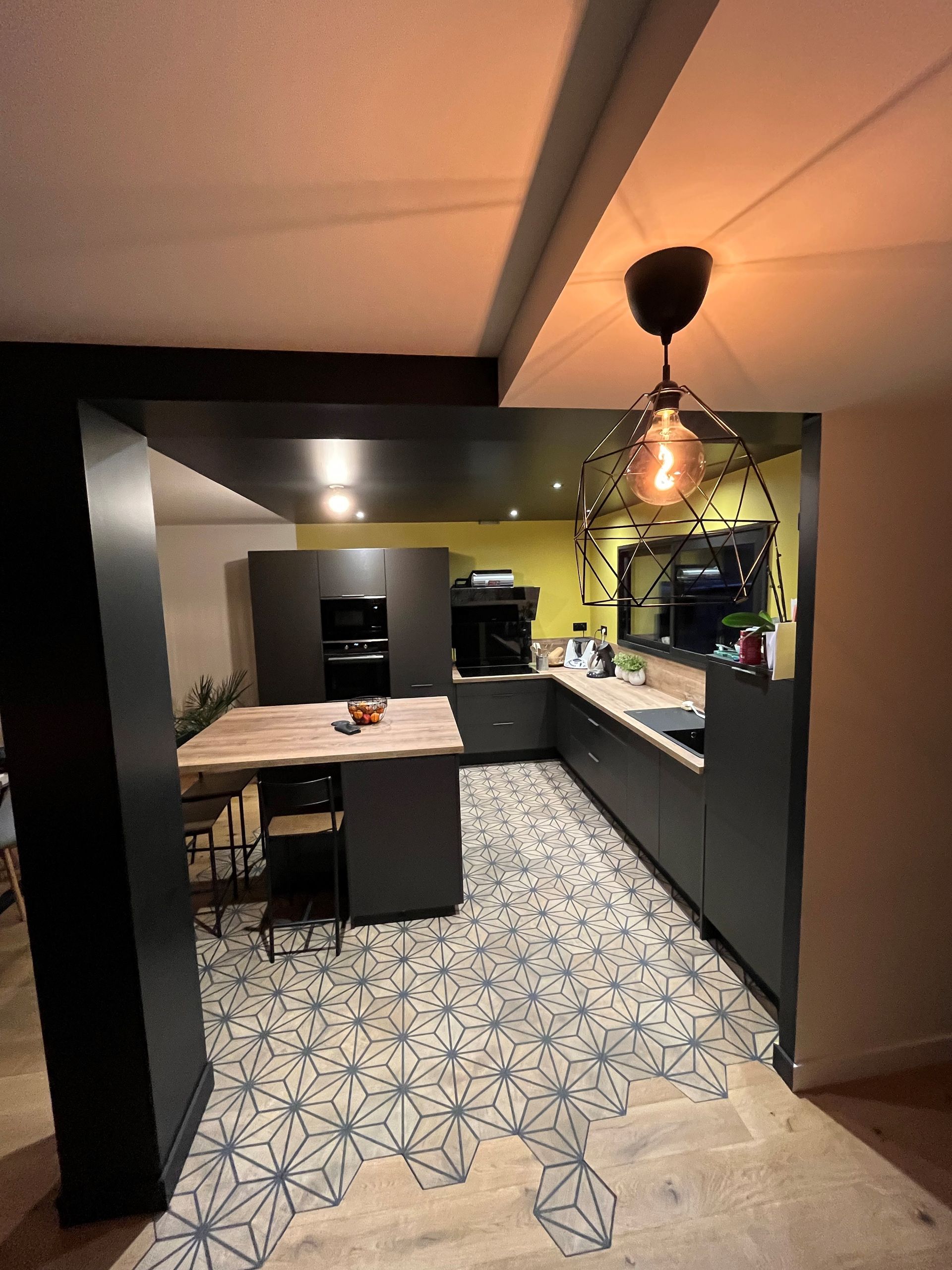 Cuisine moderne avec sol carrelé à motifs, placards foncés, suspension lumineuse et table à manger
