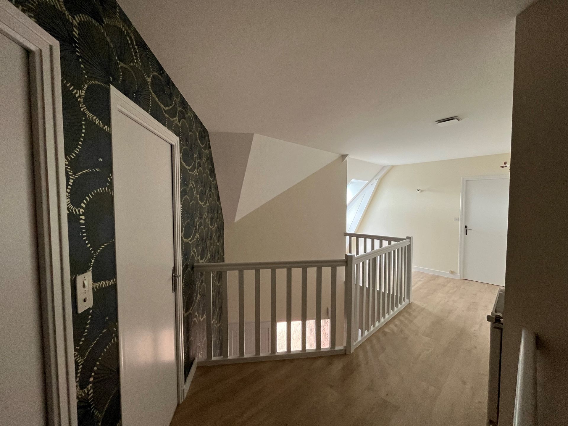 Palier d'escalier dans un couloir moderne avec rampes blanches, parquet et mur d'accent à motifs foncés.