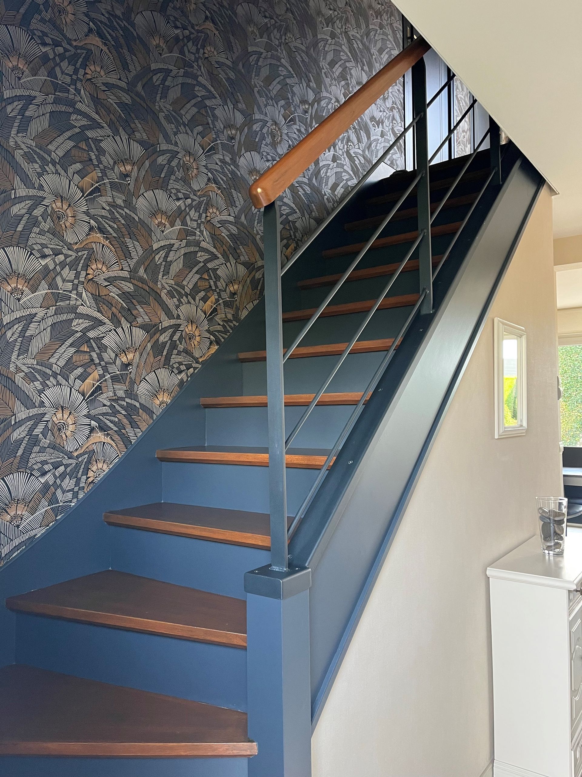 Escalier intérieur moderne avec rampes bleues, marches foncées et papier peint à motifs.