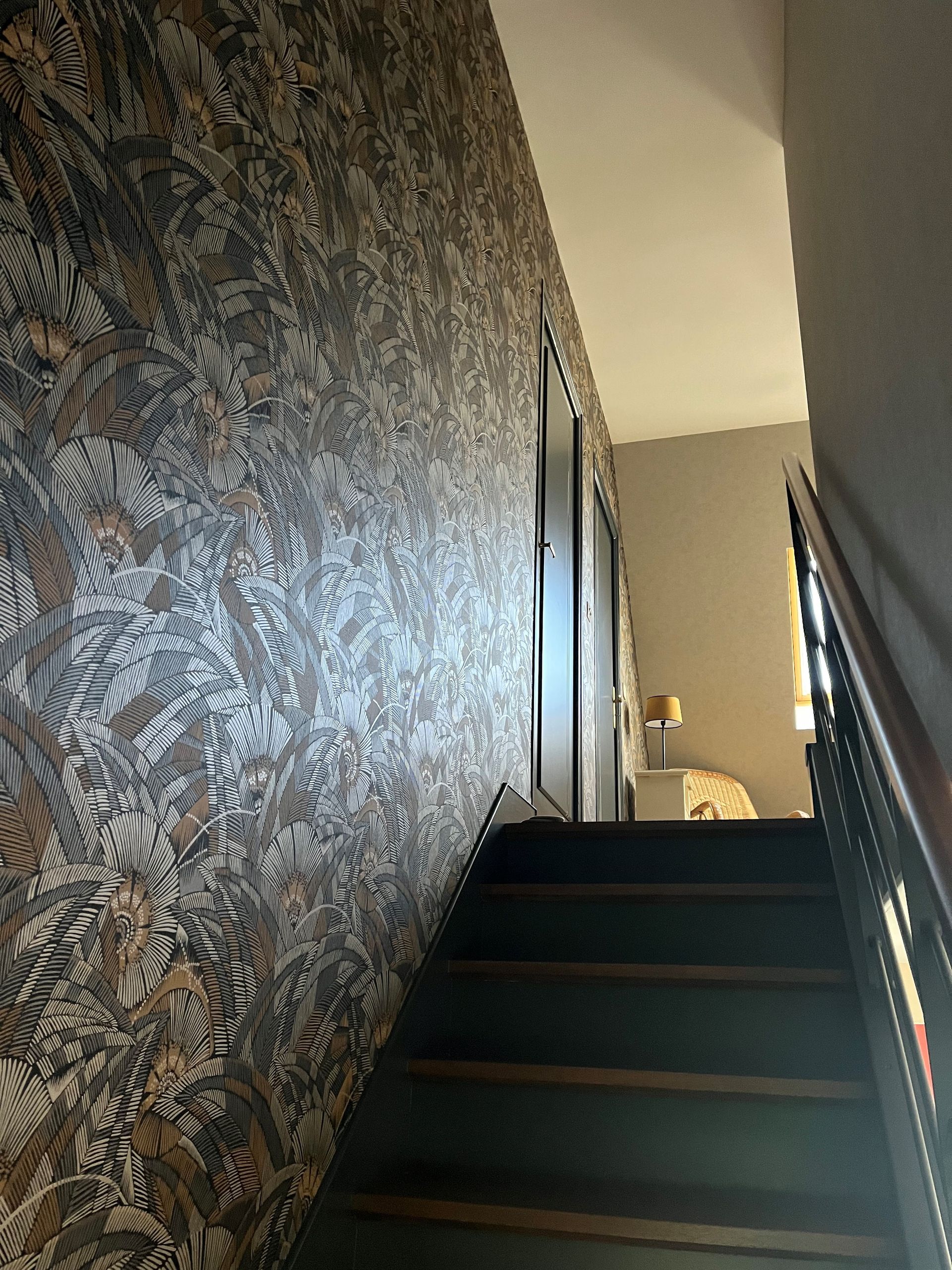 Escalier étroit recouvert de moquette, avec papier peint à motifs et rampe, dans un couloir sombre.