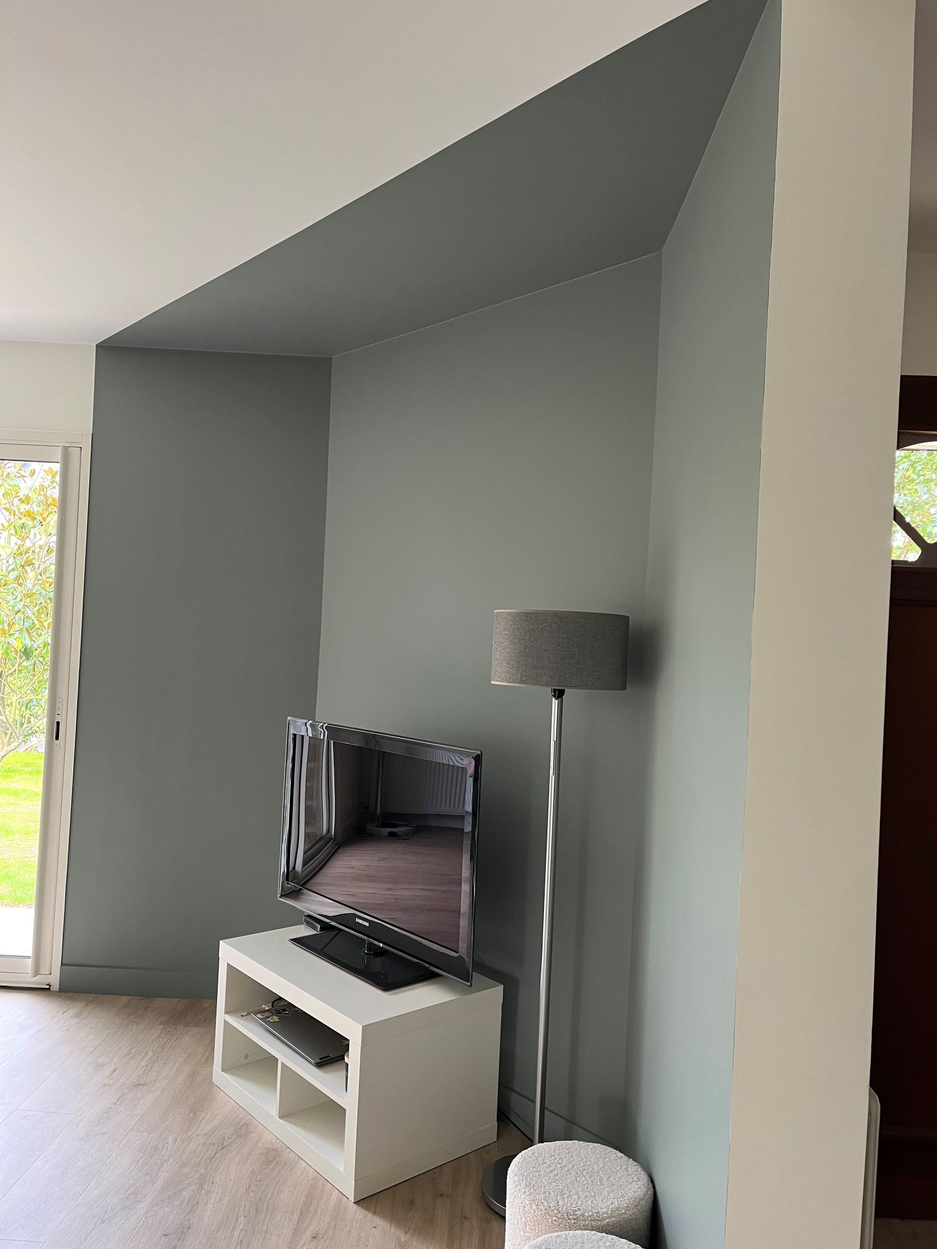 Coin salon avec murs gris, télévision sur meuble blanc, lampadaire et petit pouf