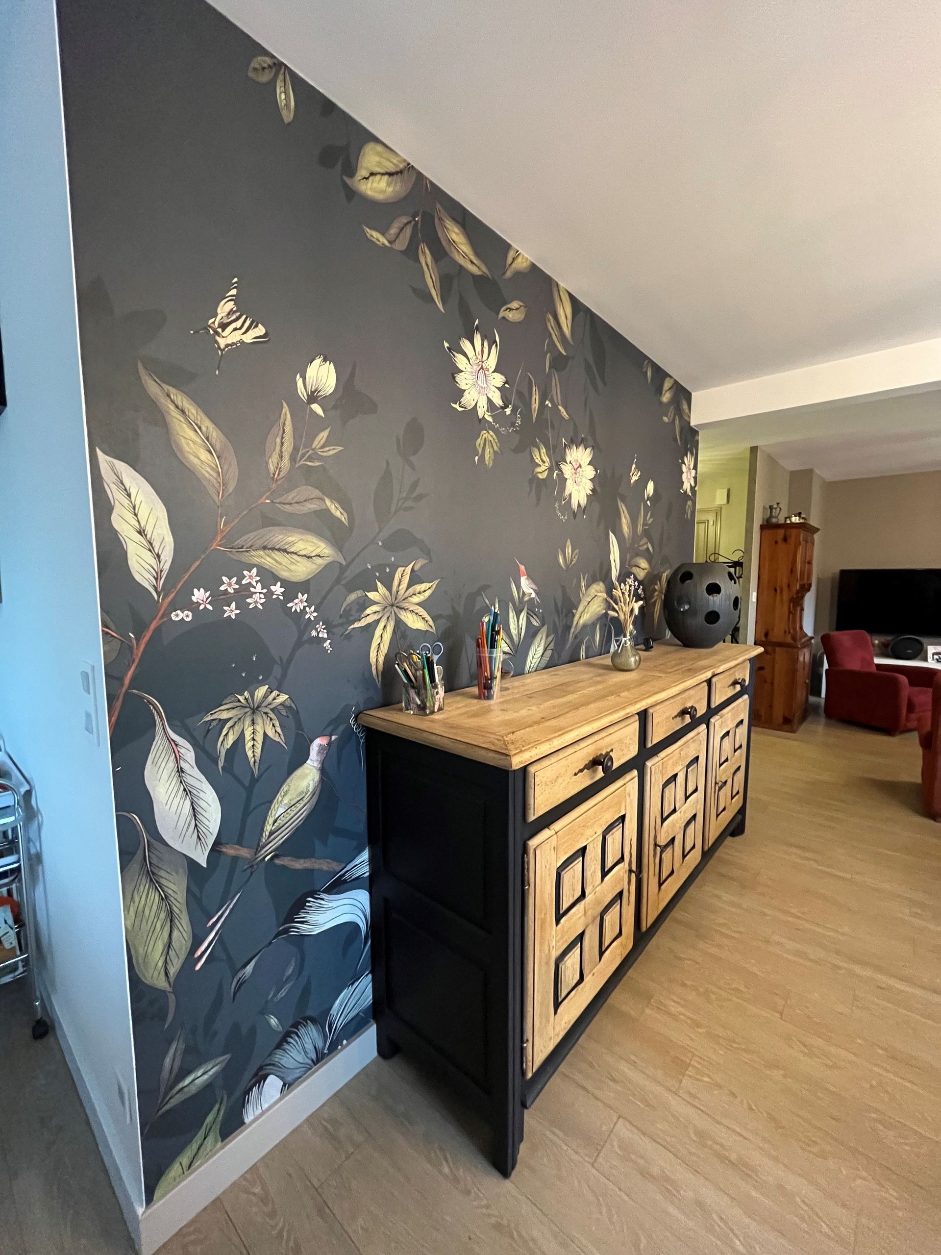 Mur recouvert de papier peint décoratif avec un buffet noir et un meuble en bois clair dans un salon