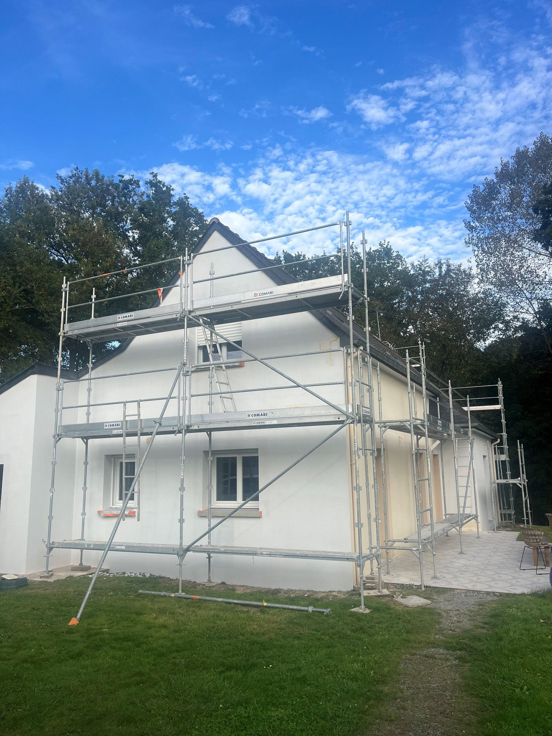 Maison blanche à deux étages avec des échafaudages en cours de rénovation extérieure sous un ciel bleu