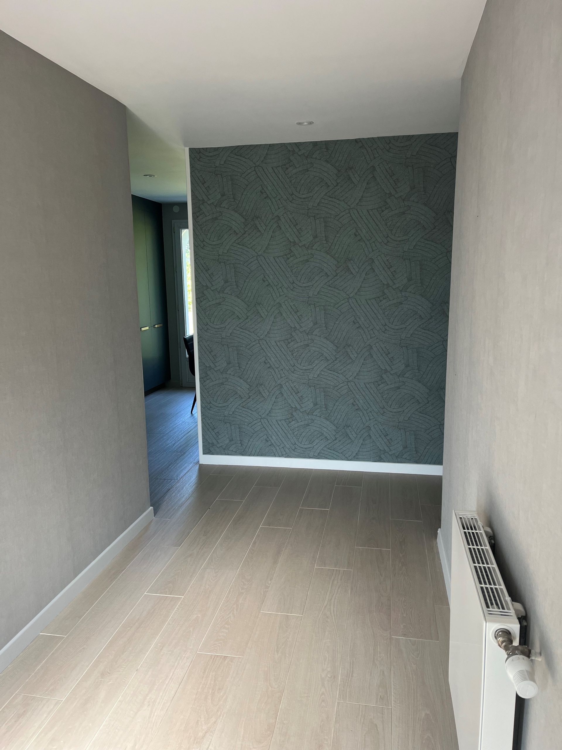 Couloir étroit et vide, avec des murs beiges, un mur d'accent gris et un radiateur blanc sur la droite.