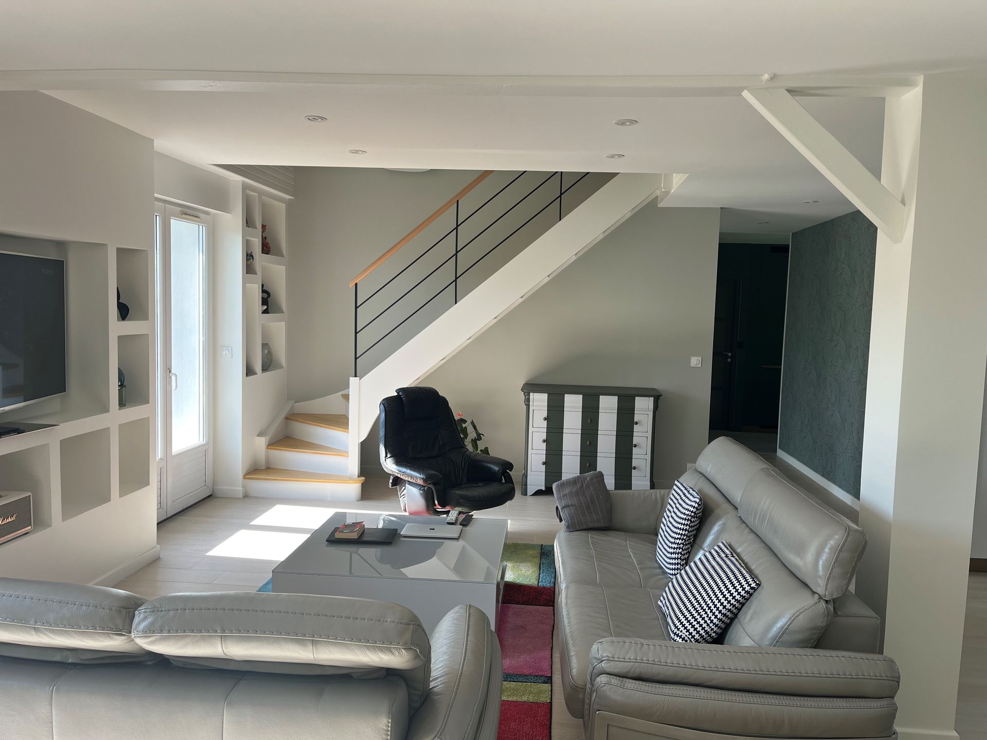 Salon moderne avec canapés gris, escalier et lumière naturelle entrant par les fenêtres