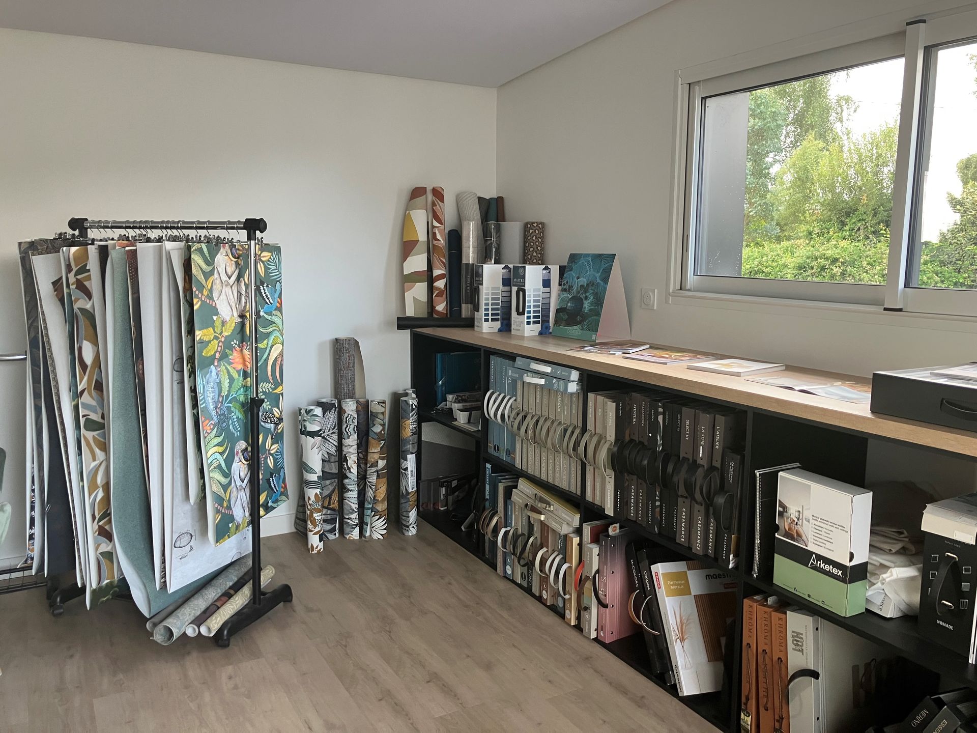 Des rouleaux de tapisserie et des fournitures sont disposés le long d'un mur dans un showroom